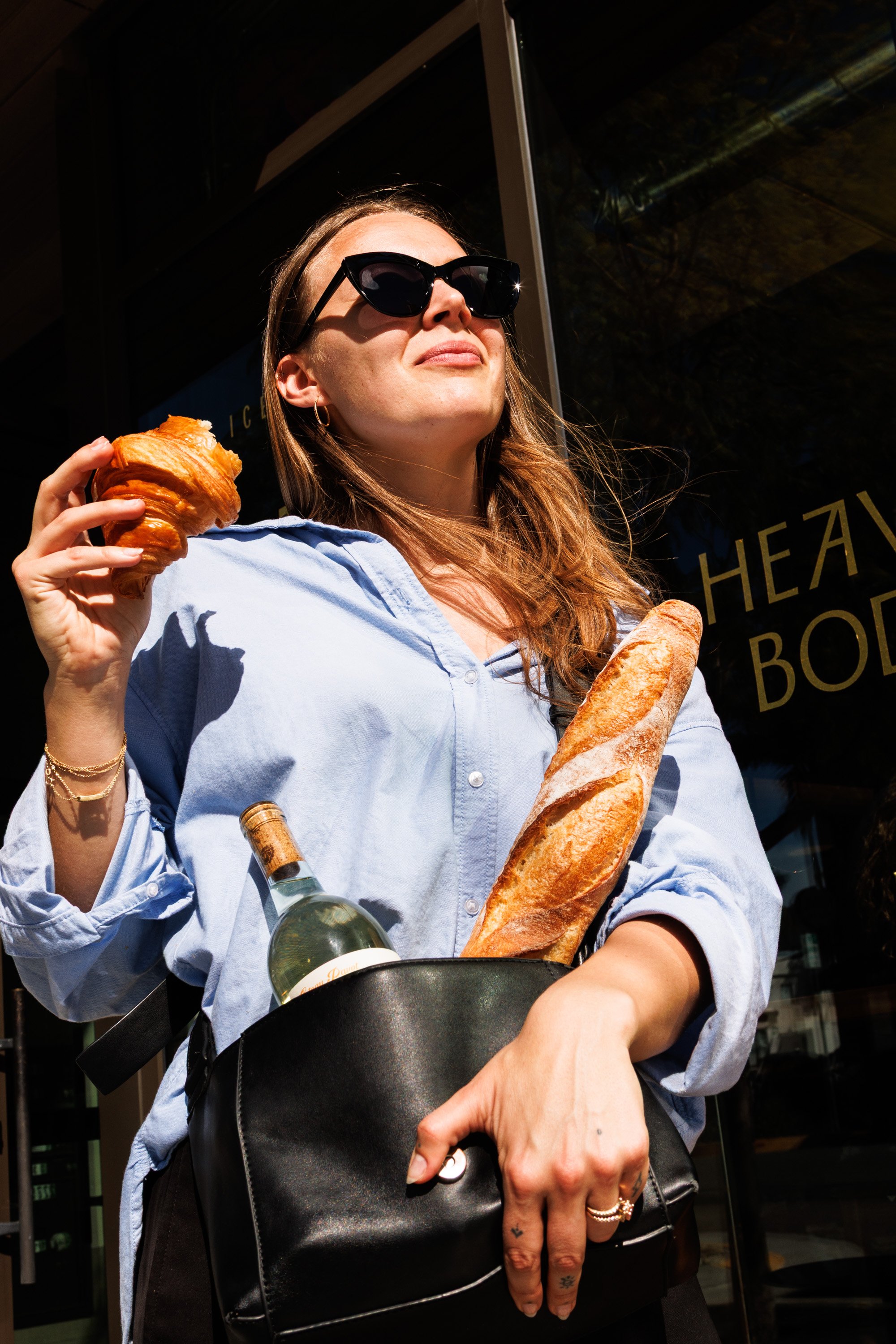 Commercial lifestyle photo for a hospitality brand campaign featuring a woman smiling with bread and wine in her purse.