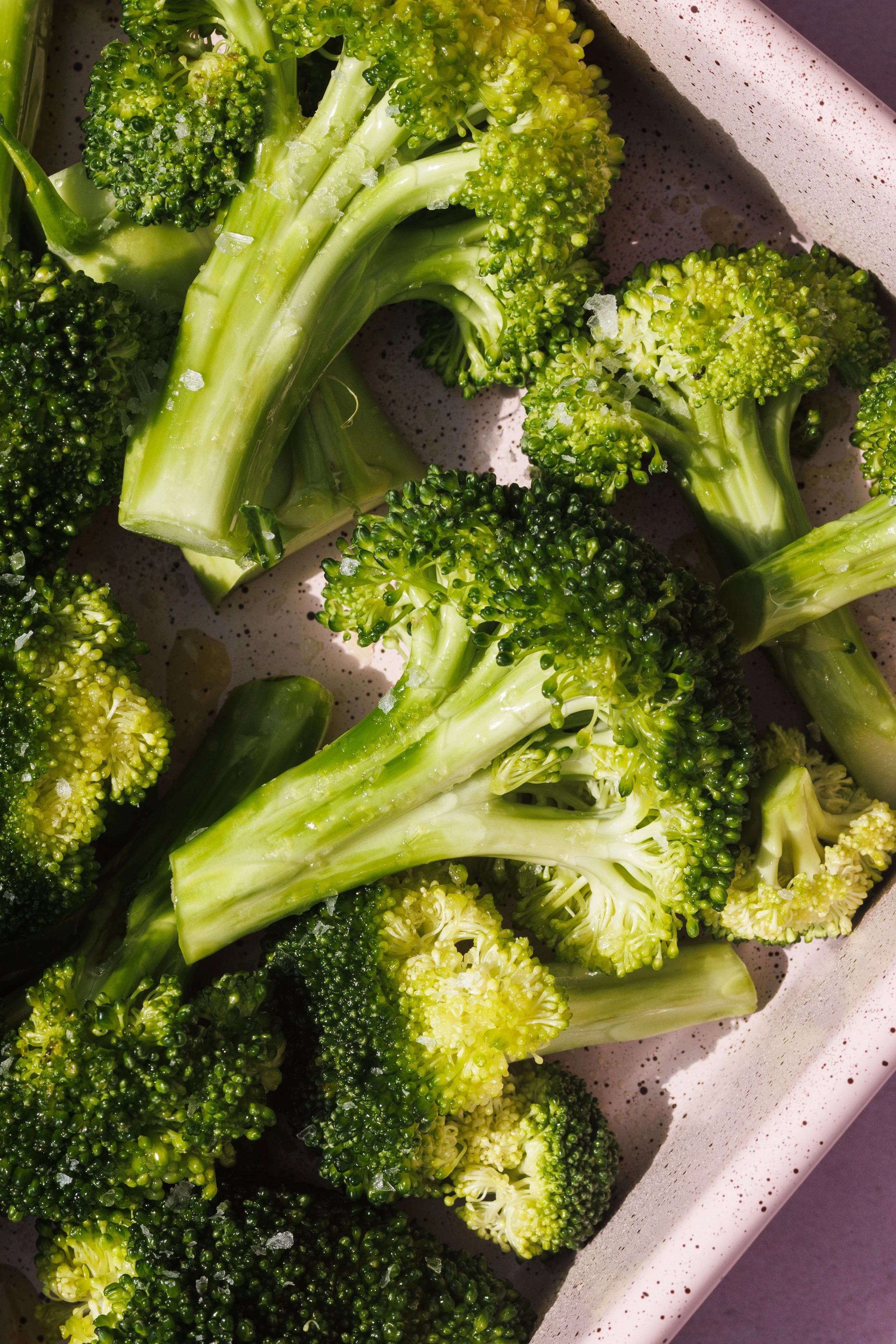 Commercial food photo of broccoli florets on a speckled baking sheet.