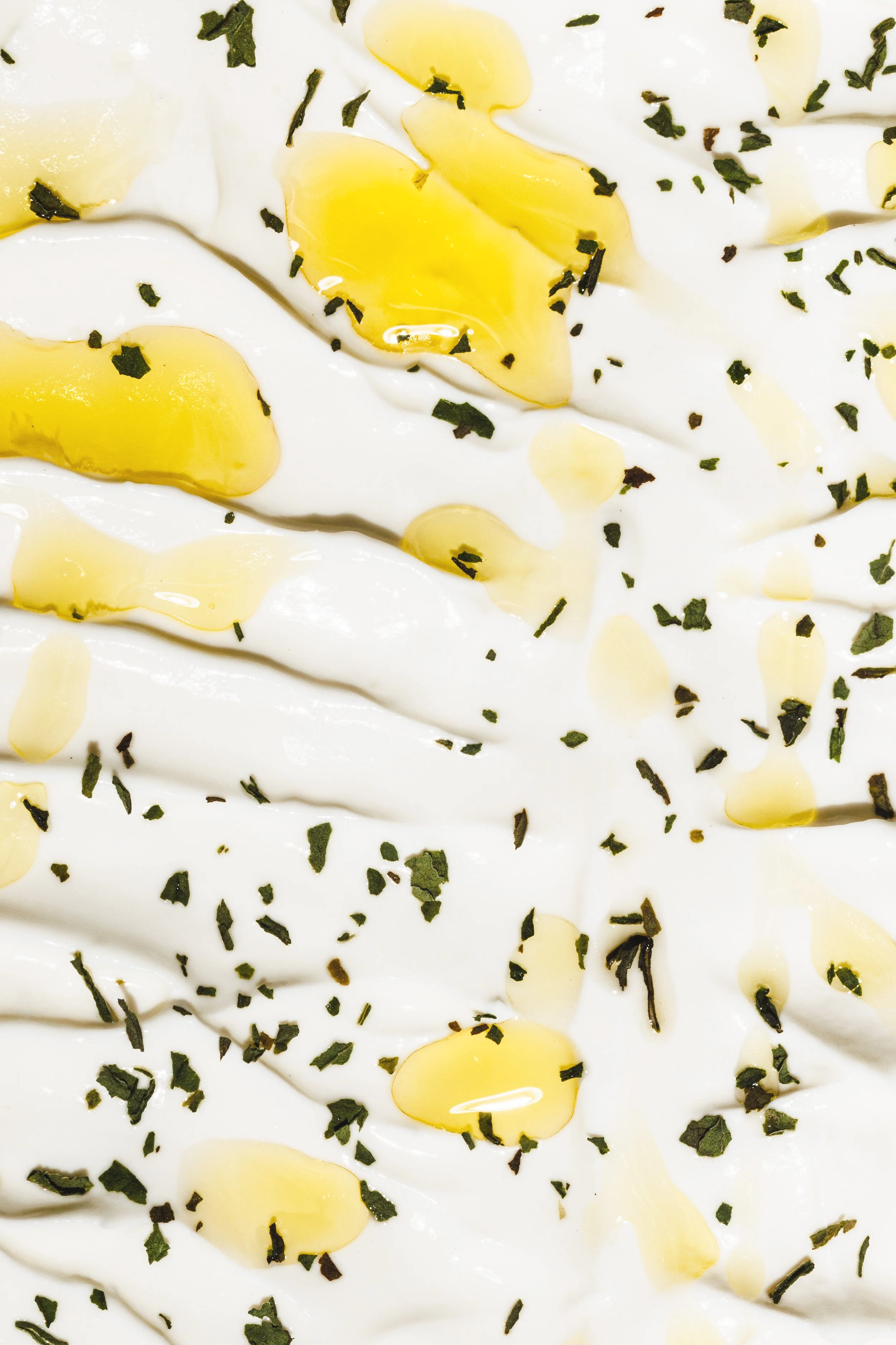 Commercial food photo of a creamy yogurt sauce with olive oil and herbs around, shot for a hospitality campaign by Amy Carson.