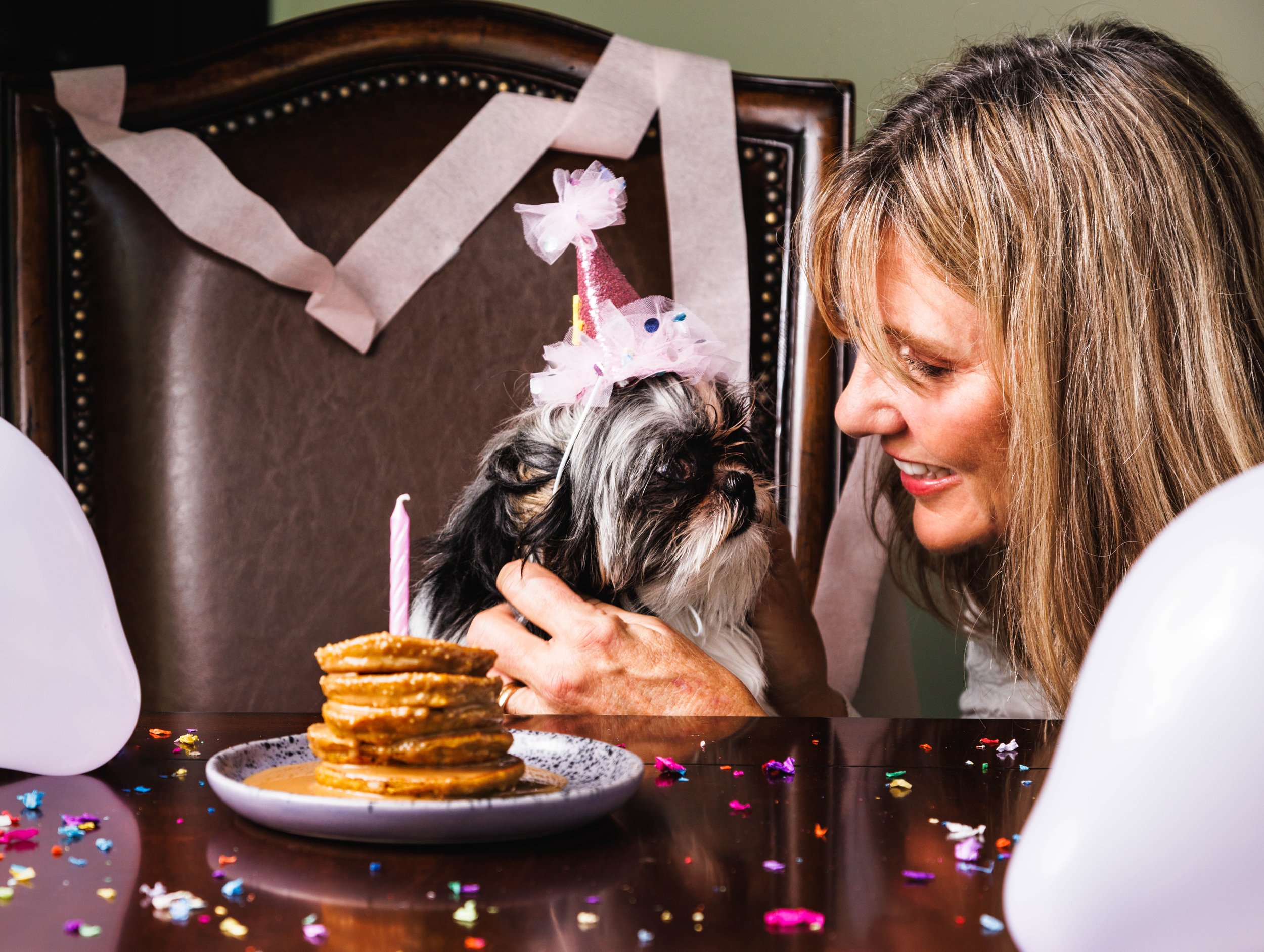 Commercial lifestyle photo of a woman and her dog in a party hat with pancakes for a brand campaign.