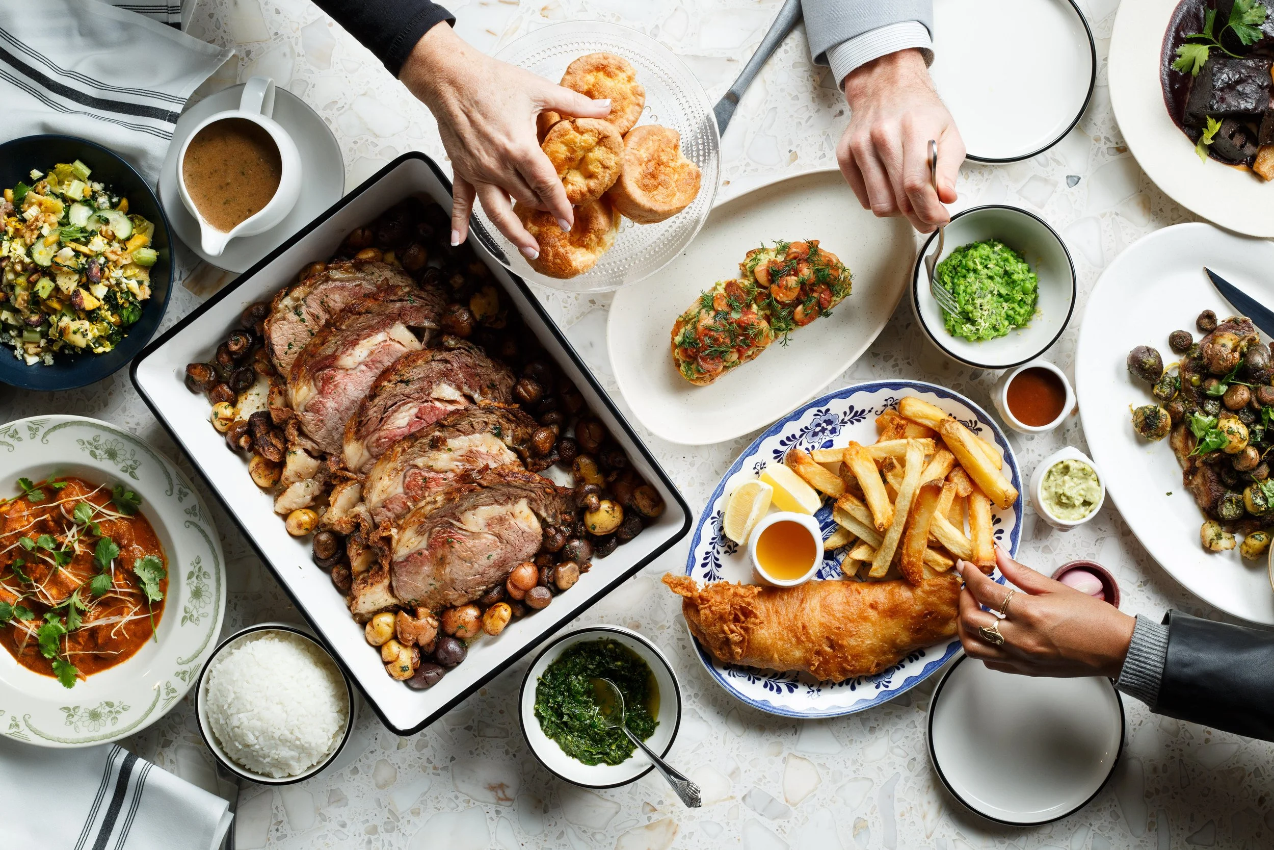 Commercial lifestyle hospitality photo of a banquet table in a restaurant full of food, with hands reaching into frame.