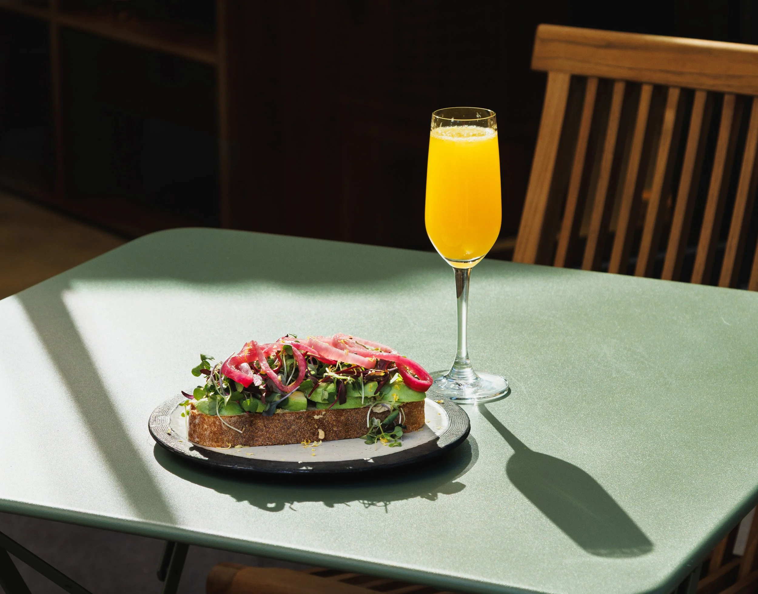 Commercial food photo of avocado toast and a mimosa on a green table for a hospitality brand campaign, by Amy Carson.