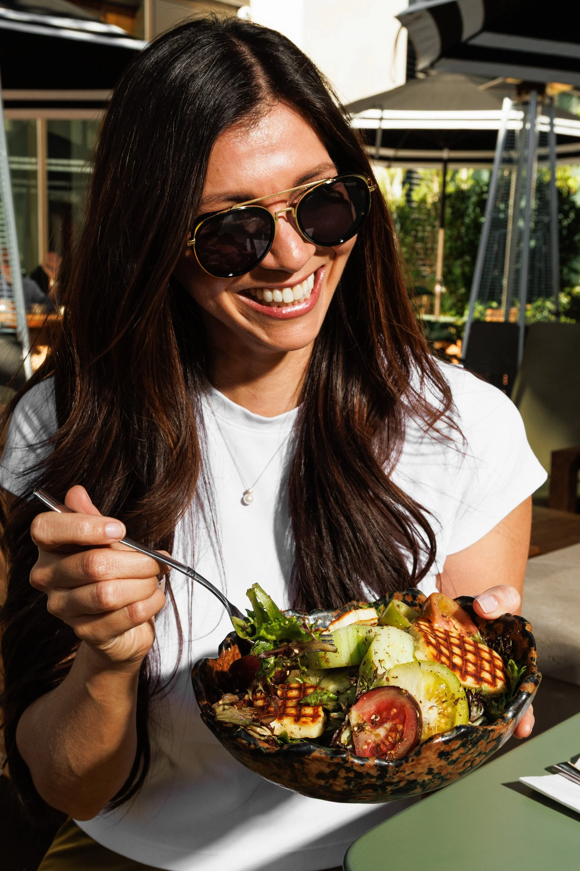 Commercial lifestyle photo of a woman eating a salad on a patio in San Diego for a hospitality brand campaign.