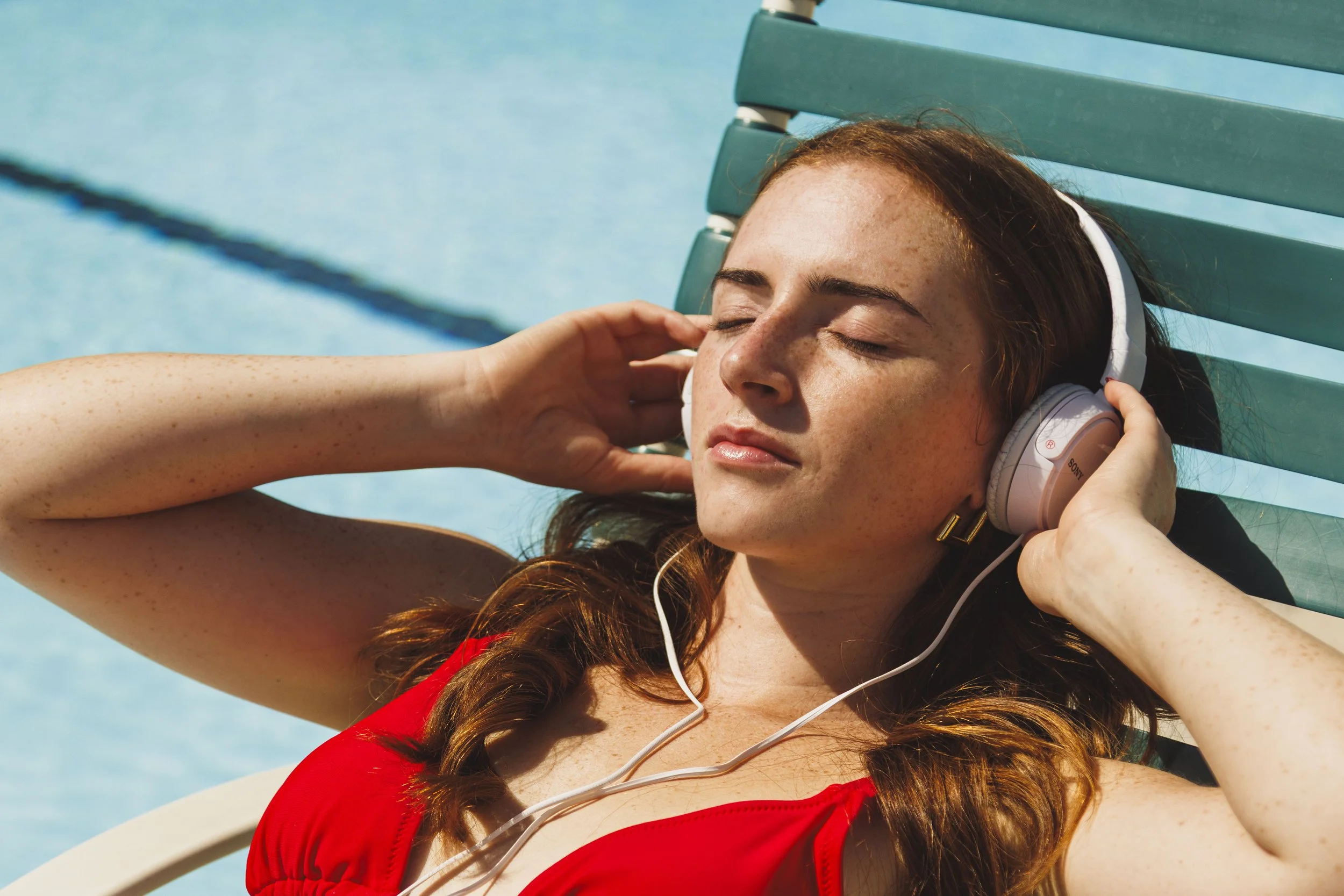 Commercial lifestyle photo of a woman listening to headphones by the pool in Los Angeles, California.