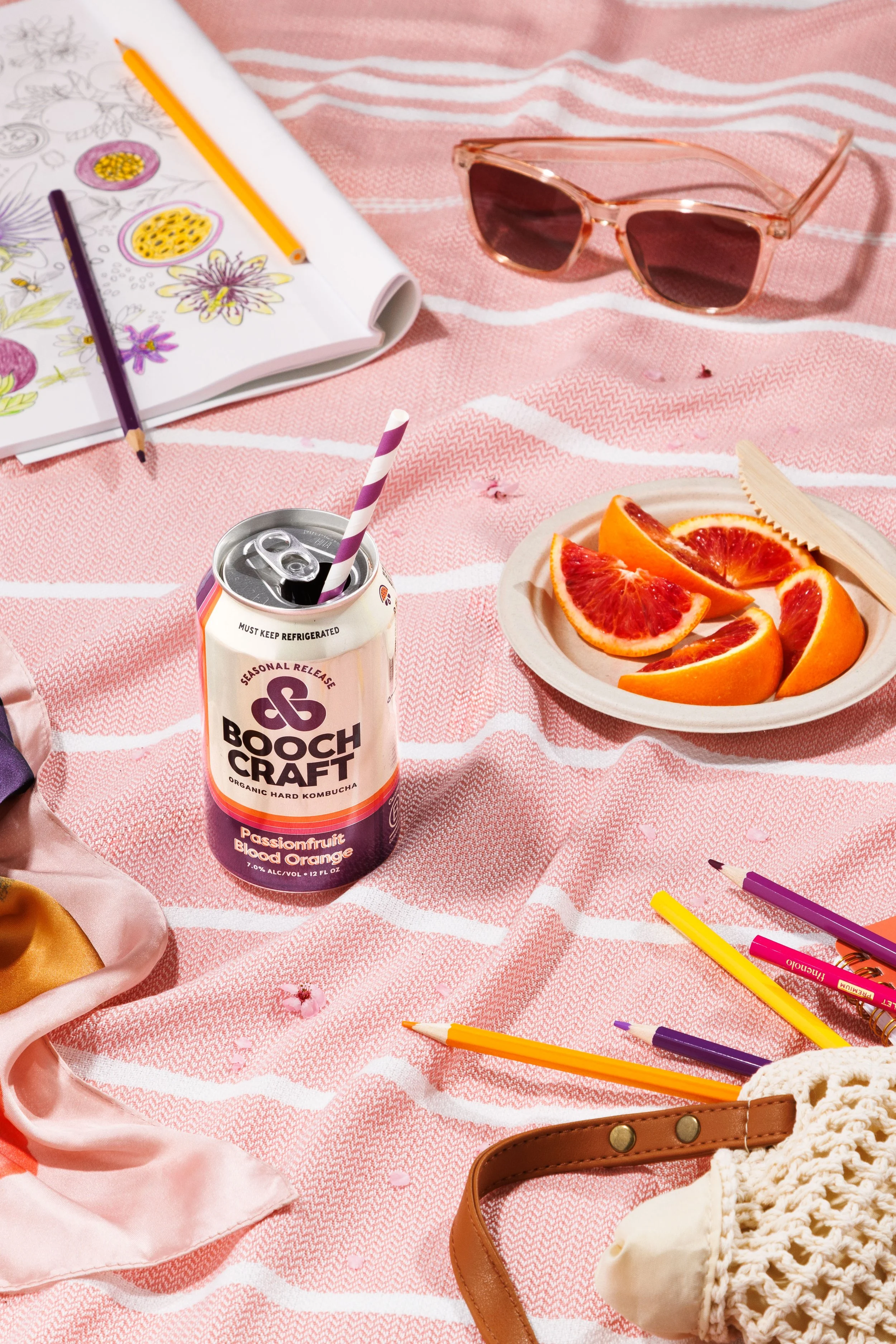 Commercial lifestyle beverage photo of a canned kombucha, colored pencils and sunglasses in a spring-themed scene.