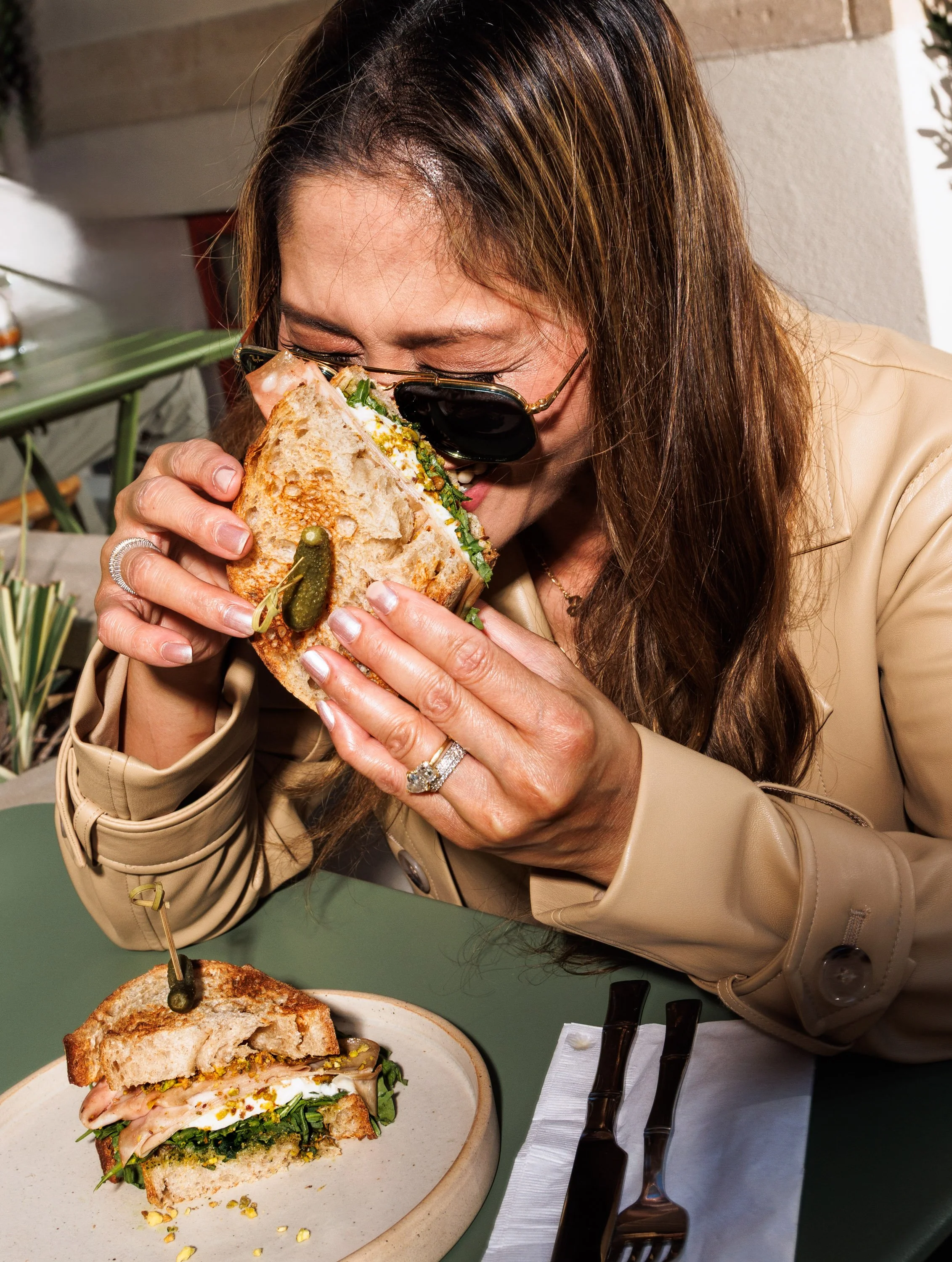 Commercial food photo of a woman holding a sandwich and laughing for a branded hospitality campaign.