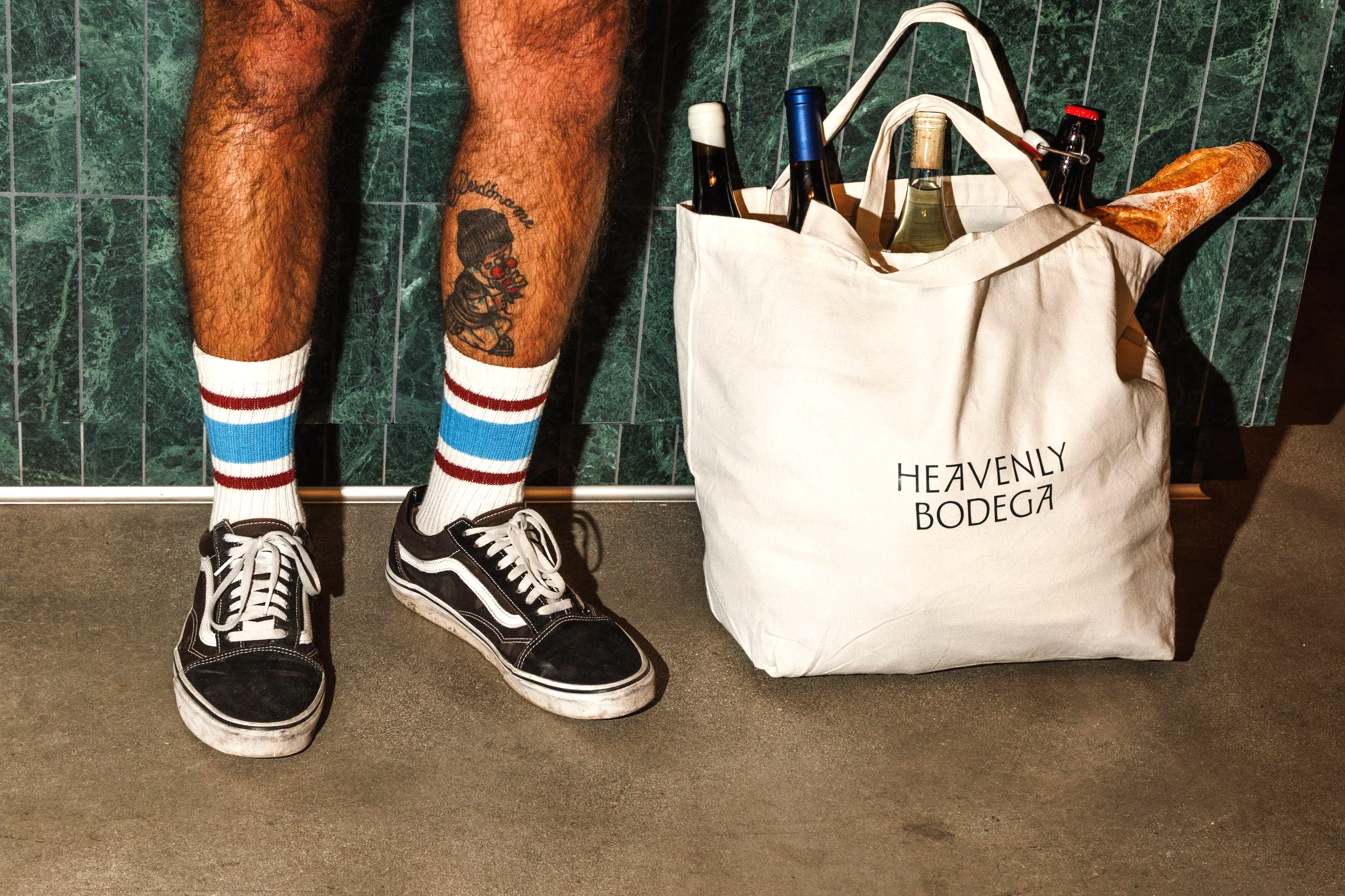 Commercial lifestyle photo of a man's legs with a canvas bag full of wine and bread for a branded campaign.