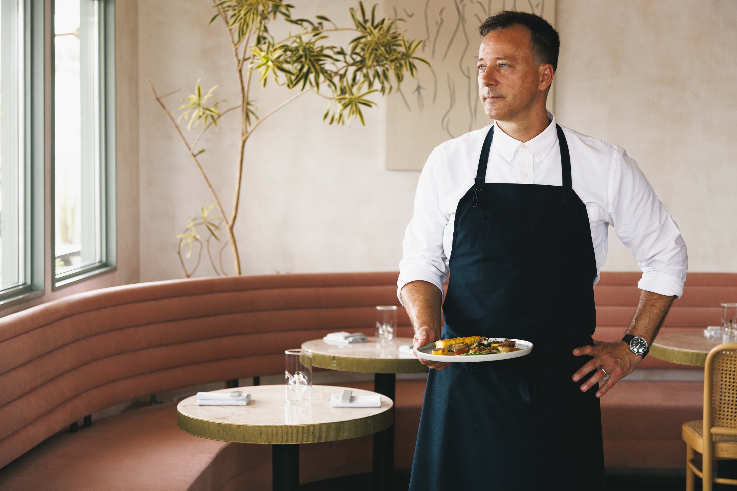 Editorial portrait of a chef holding a plate with restaurant interiors visible. Shot by Amy Carson for the Los Angeles Times.