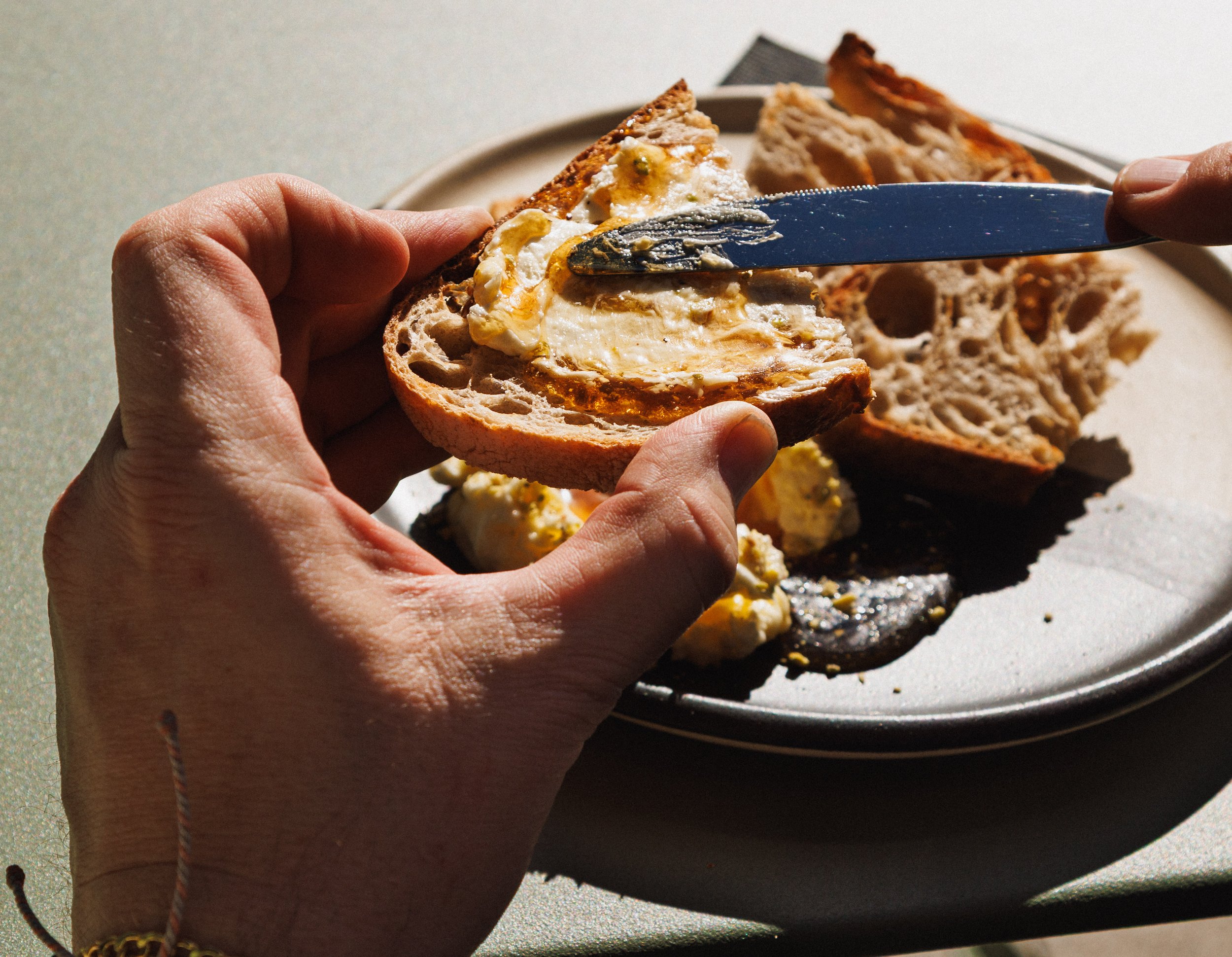 Commercial lifestyle food photo of a man spreading butter and honey on bread.