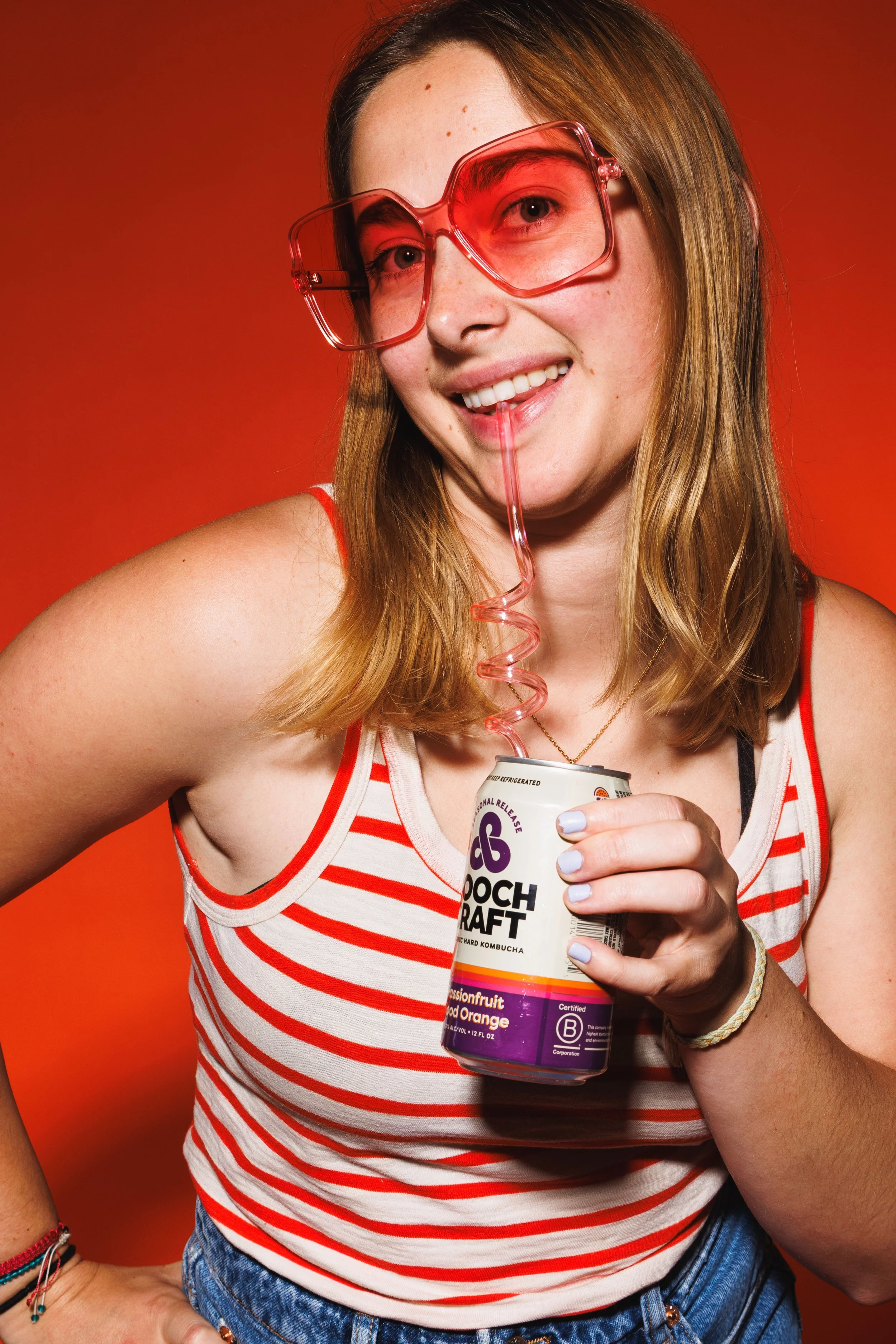 Commercial beverage lifestyle photo of a young woman drinking canned kombucha with a straw.