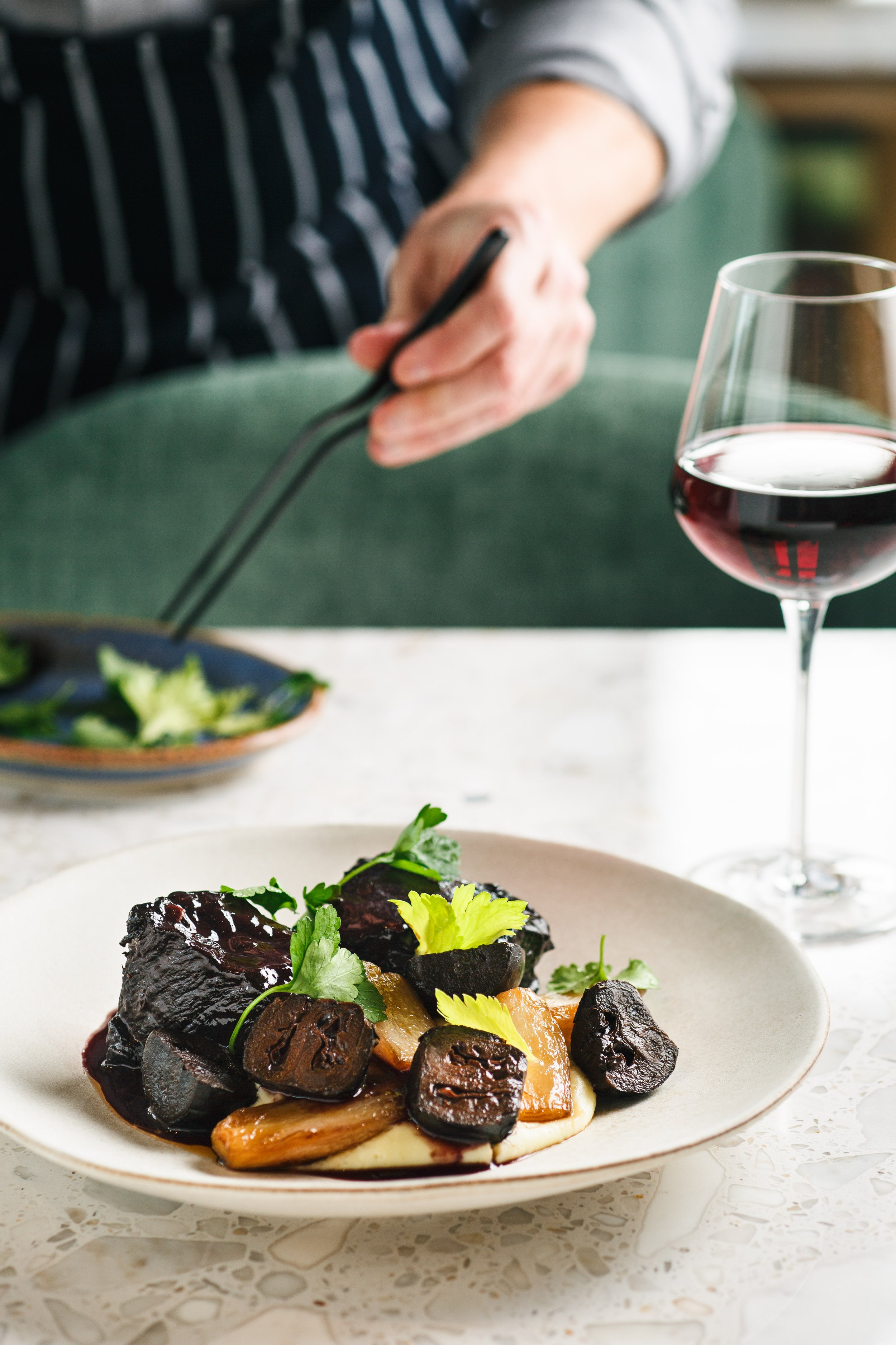 Commercial food photo of a chef plating greens on a dish.