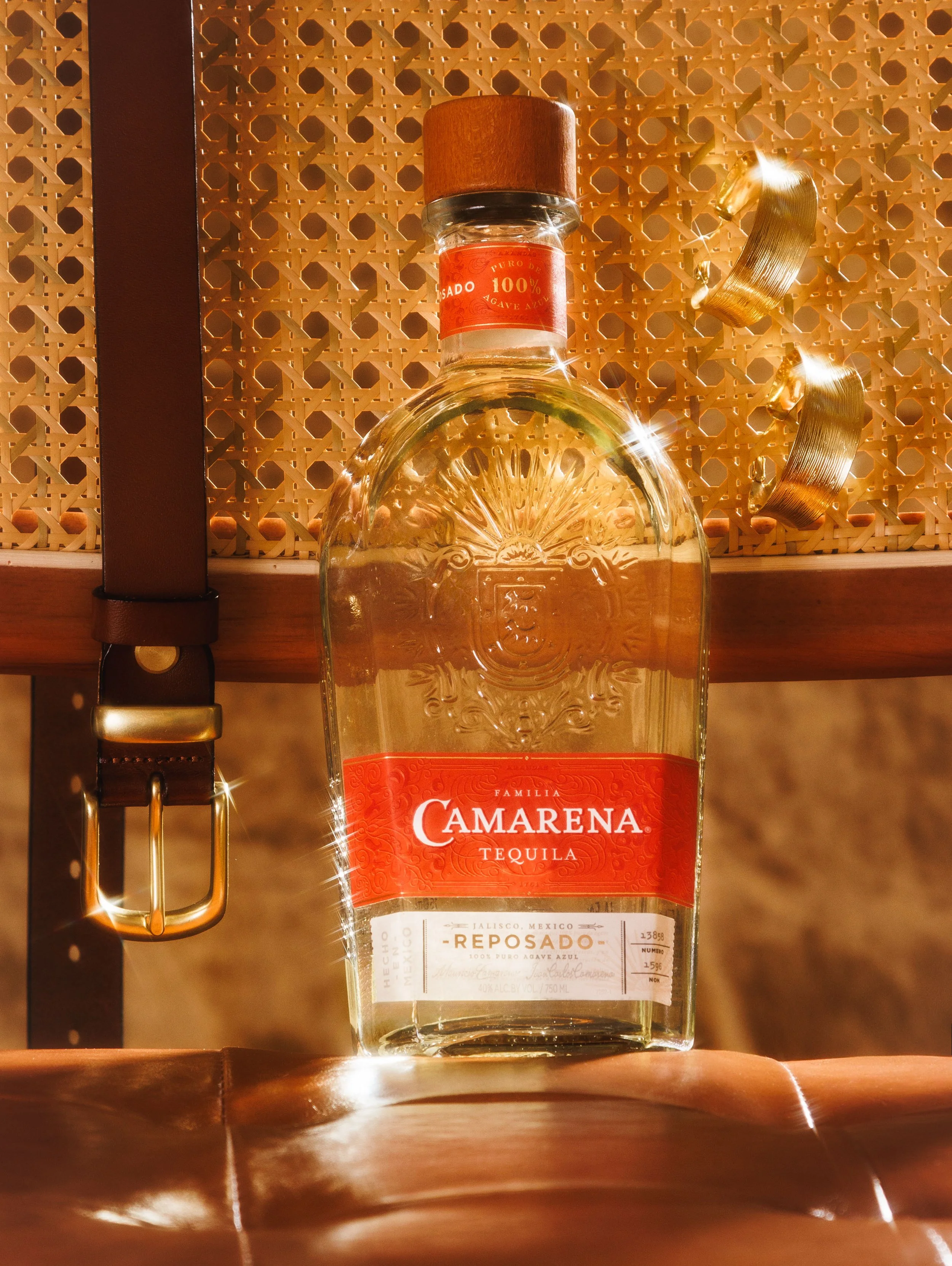 Commercial still life beverage photo of a premium tequila bottle on a leather chair with a belt and sparkly gold earrings for an advertising campaign.