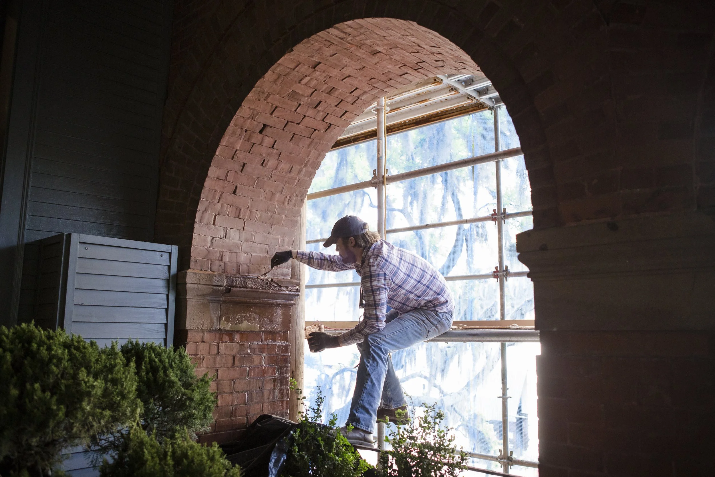 John Ecker of XIII Conservators working on brick masonry inside SCAD Poetter Hall with scaffolding and a large arched opening.
