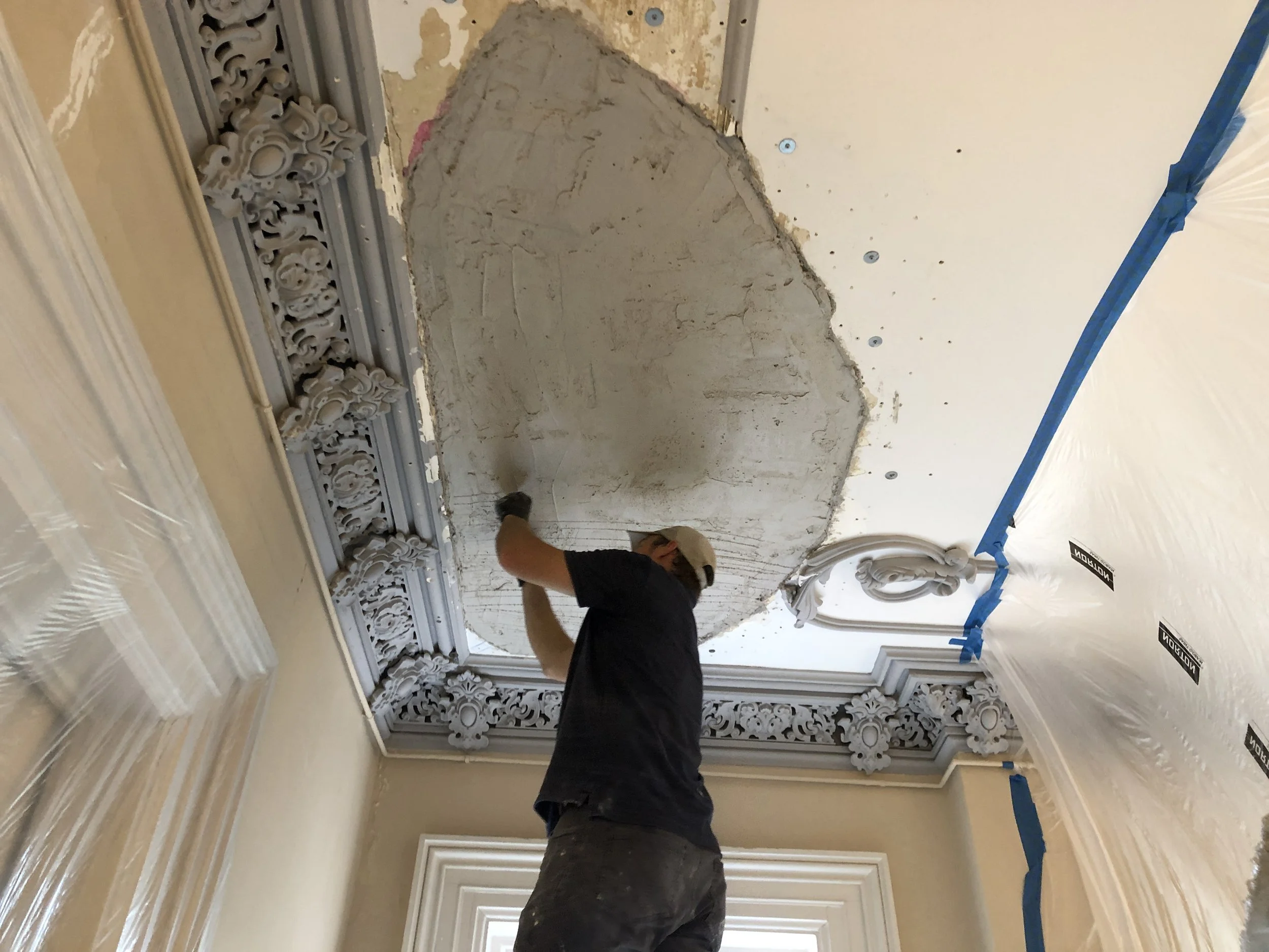 John Ecker repairing a damaged section of ornate crown molding and ceiling.