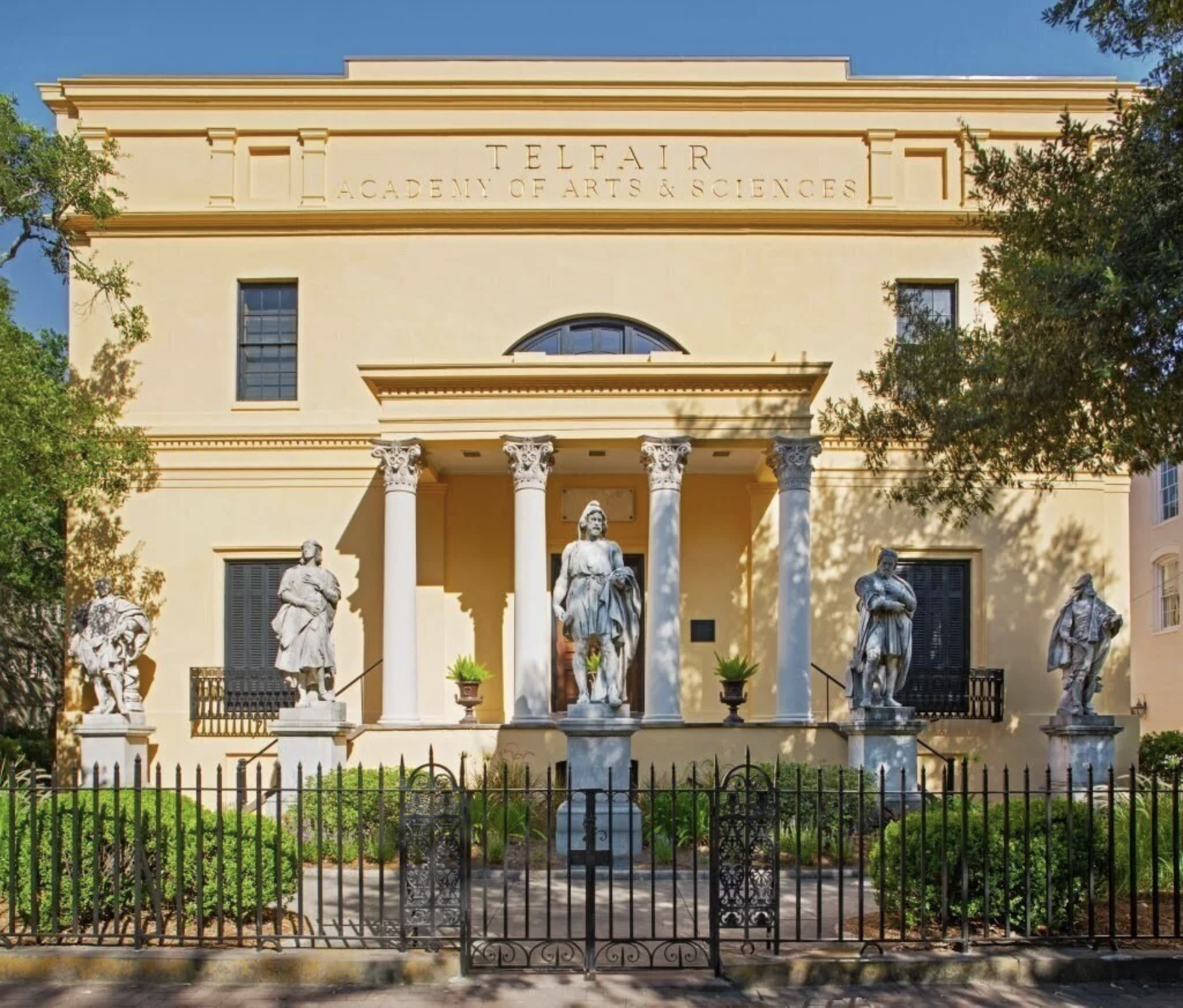 Front view of Restored Telfair Academy of Arts and Sciences building with statues in front and a black iron fence in the foreground.