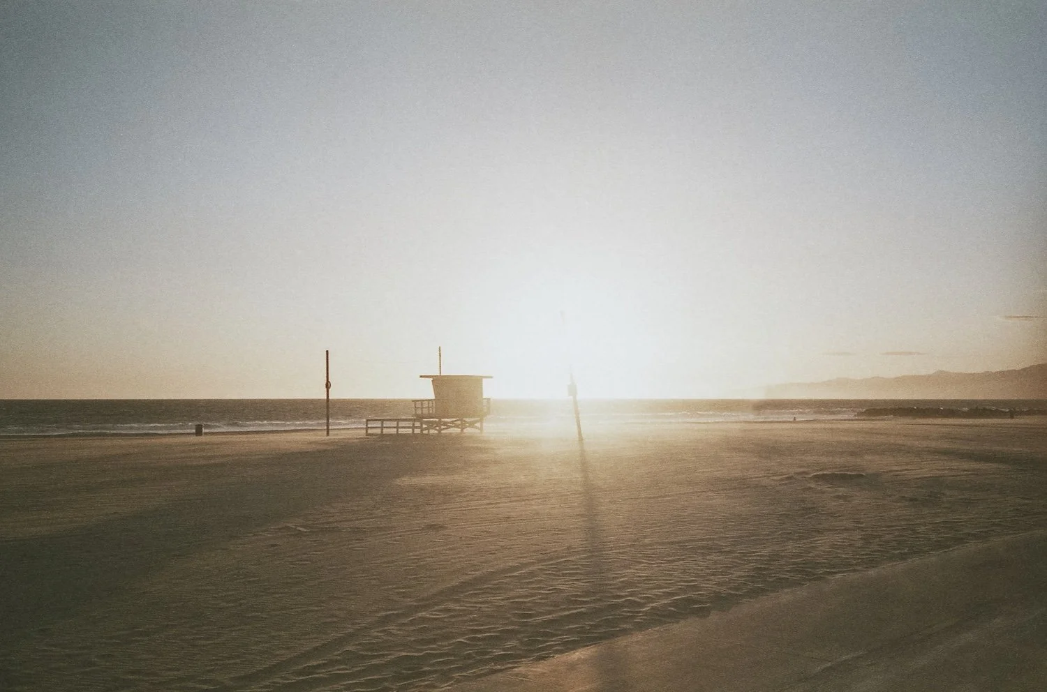 Sunset over empty beach with lifeguard tower and footprints on sand