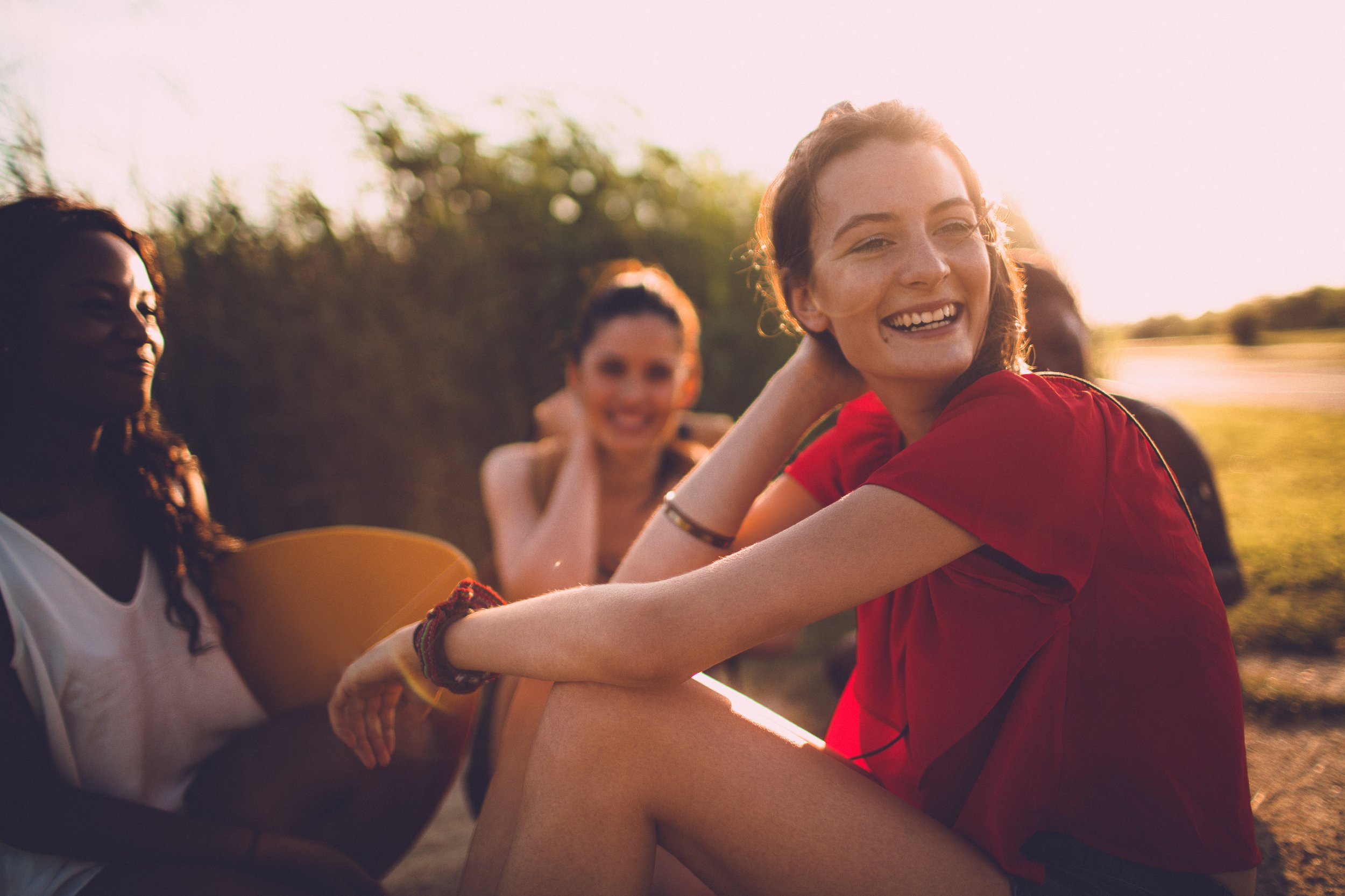 Group of young women sitting outdoors during sunset, smiling and enjoying each other's company.