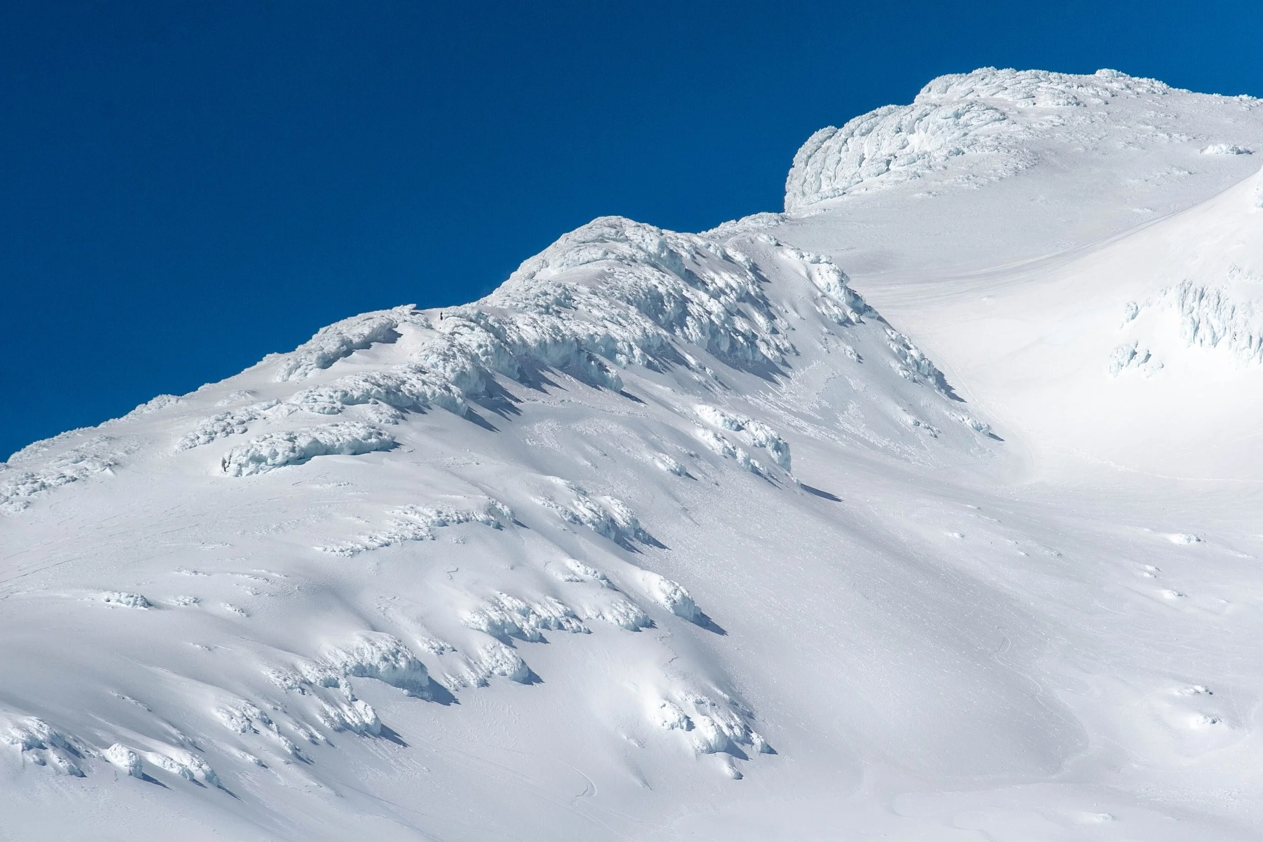 Snow-covered mountain slope with a clear blue sky in the background.