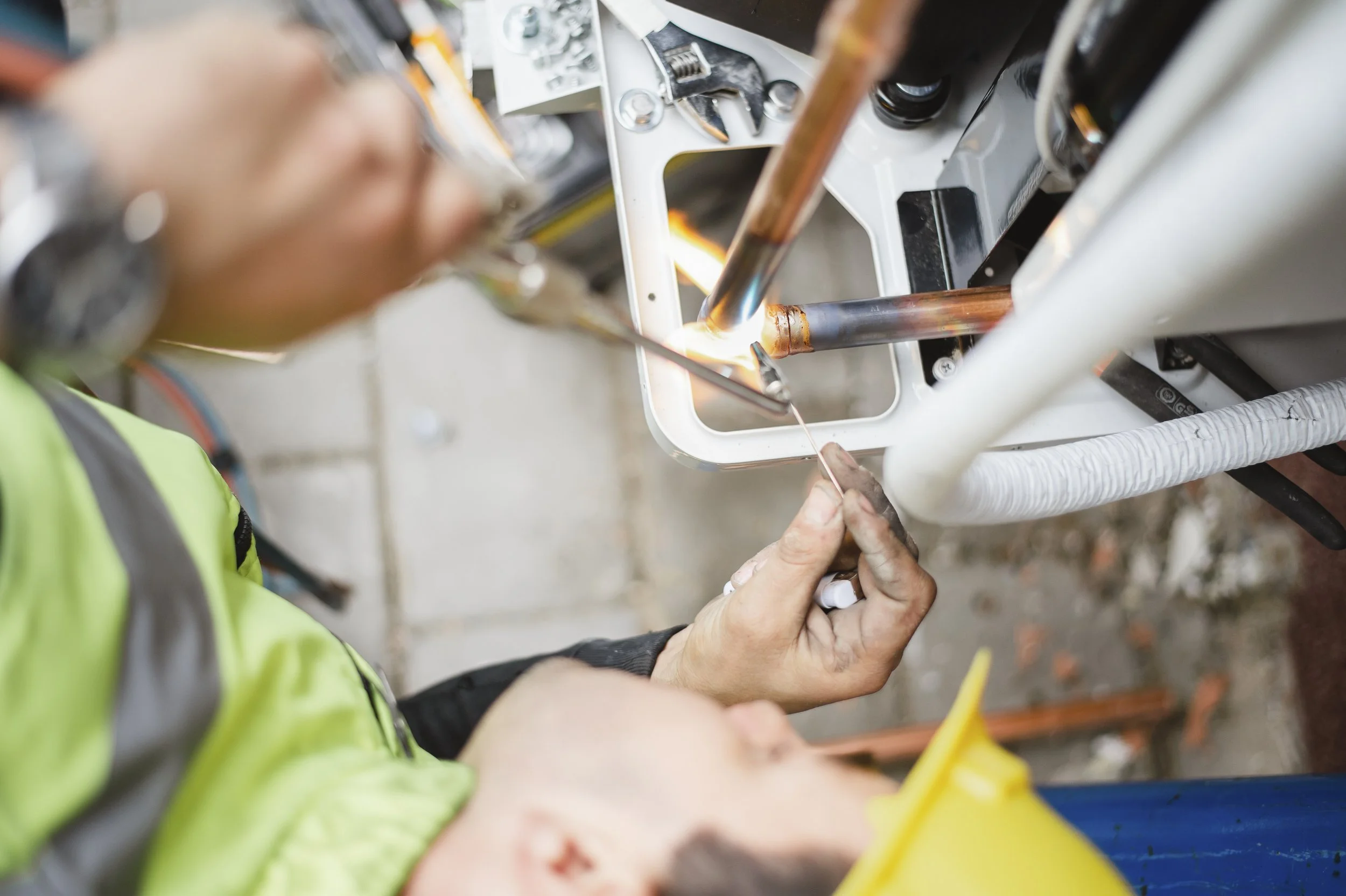 A person in a high-visibility jacket welding a metal pipe with a small torch, sparks visible.