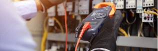 A person wearing a glove testing electrical connections with a multimeter inside an electrical panel.