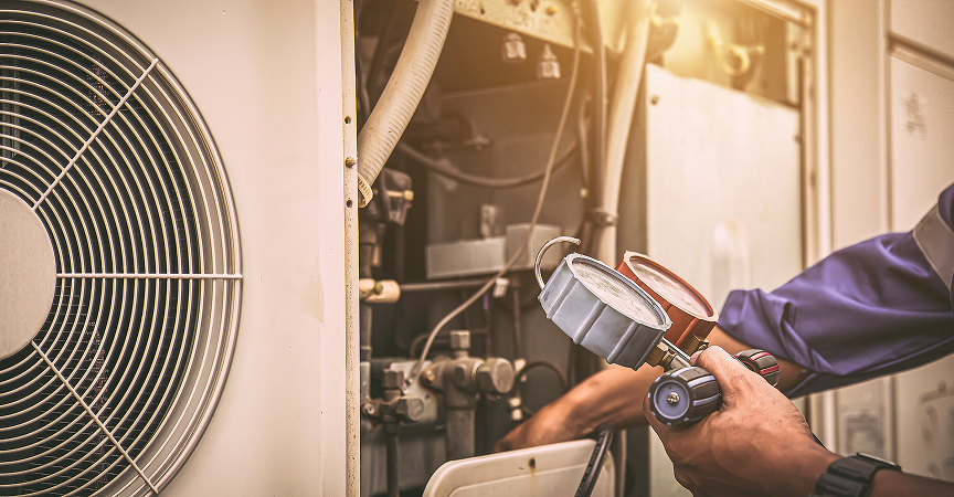 Technician inspecting or repairing an HVAC unit with gauges in hand