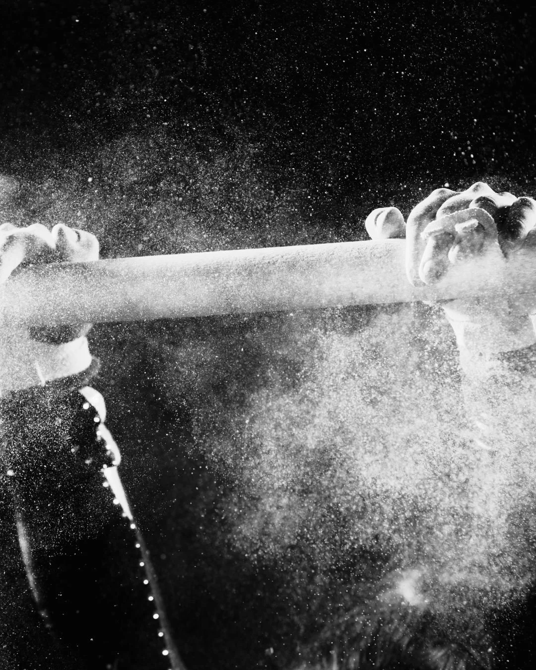 Close-up of a baseball bat being swung, hitting a ball, with powder or dust flying through the air in black and white.