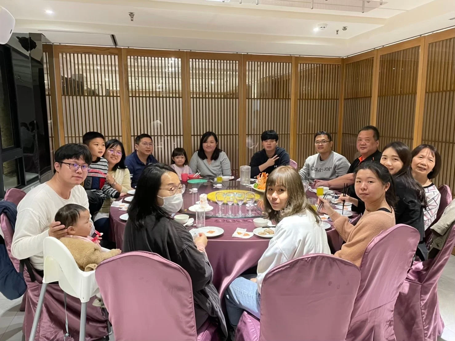 A large group of people, including children and adults, sitting around a round table in a restaurant, enjoying a meal together.