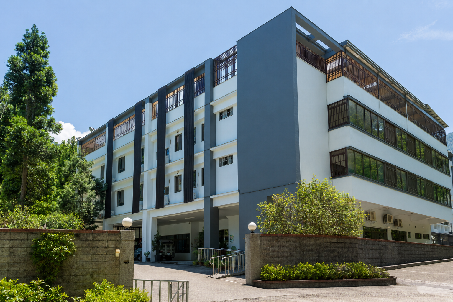 Modern multi-story building with large glass windows, surrounded by greenery and trees, under a clear blue sky.