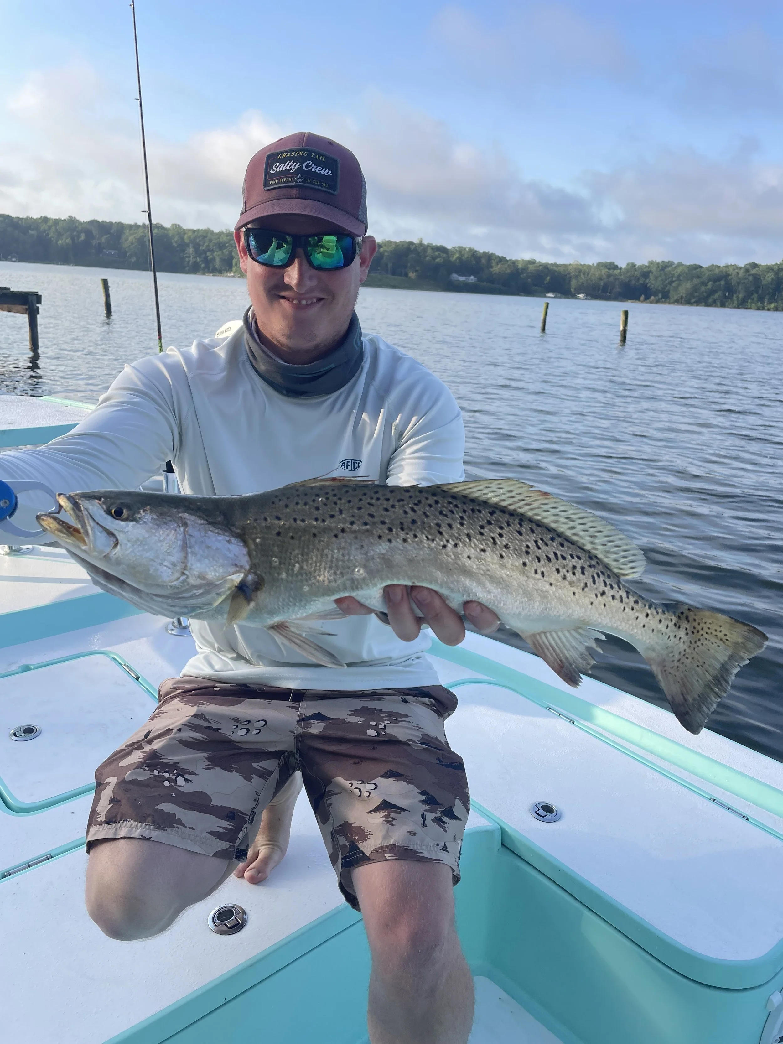 Man wearing sunglasses and a cap holding a large fish on a boat in a lake.