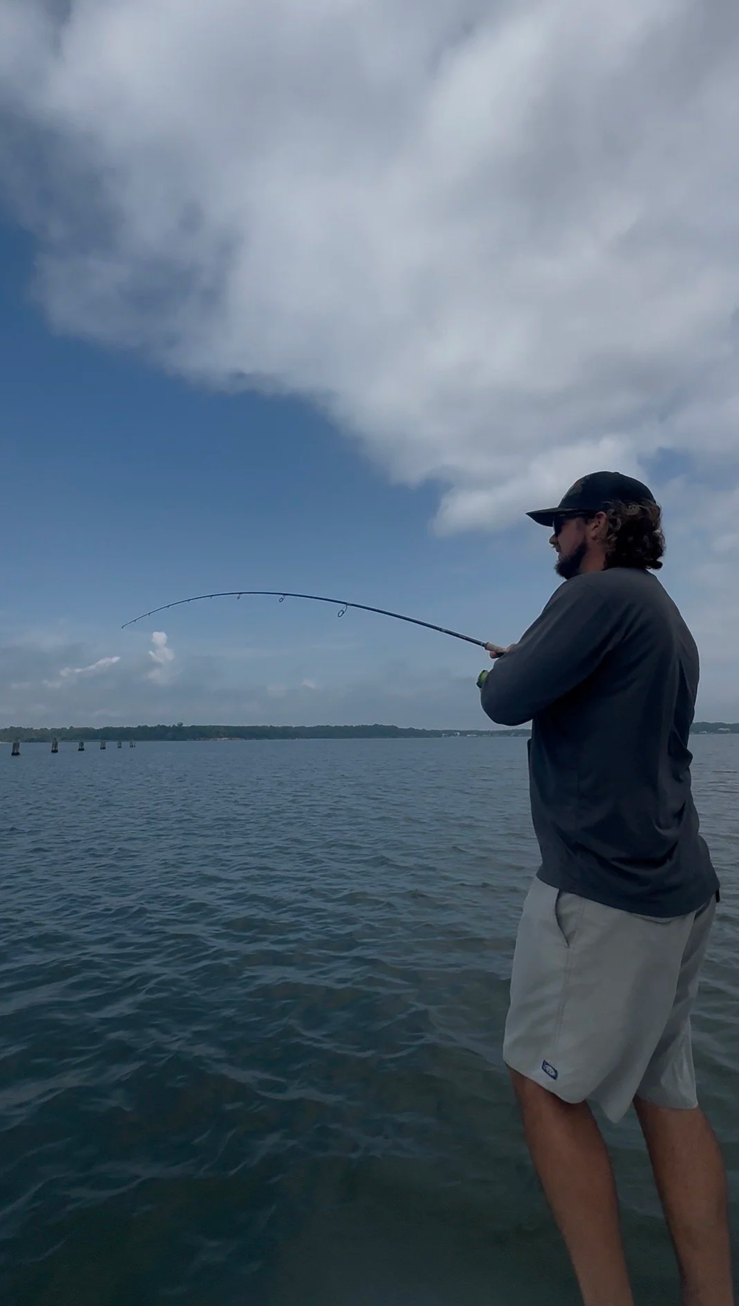 Man fishing in a large body of water during daytime with a cloudy sky.