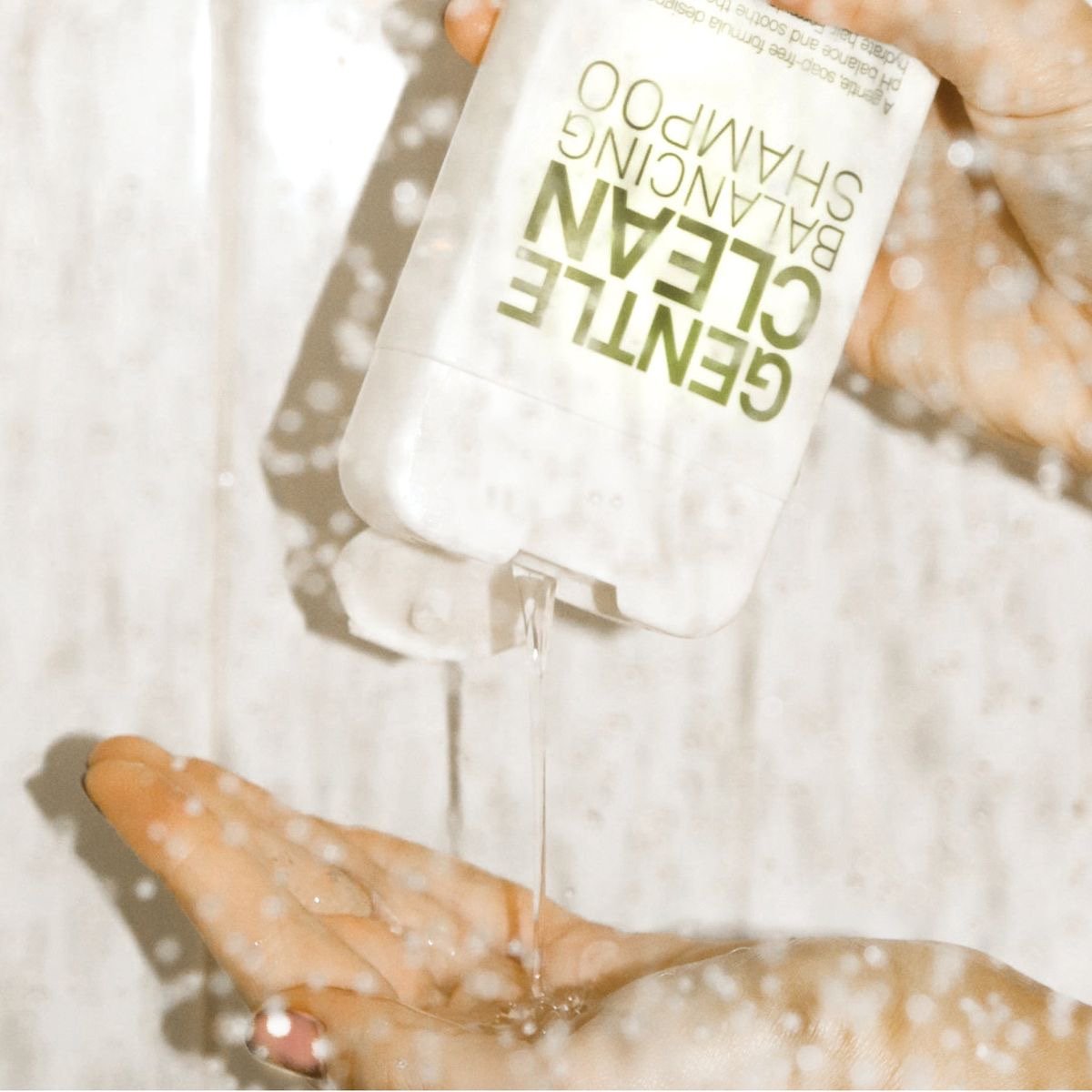 A person holding a bottle of gentle cleansing face wash above their open hand, with the product name visible on the label, and water pouring from the bottle onto their hand.