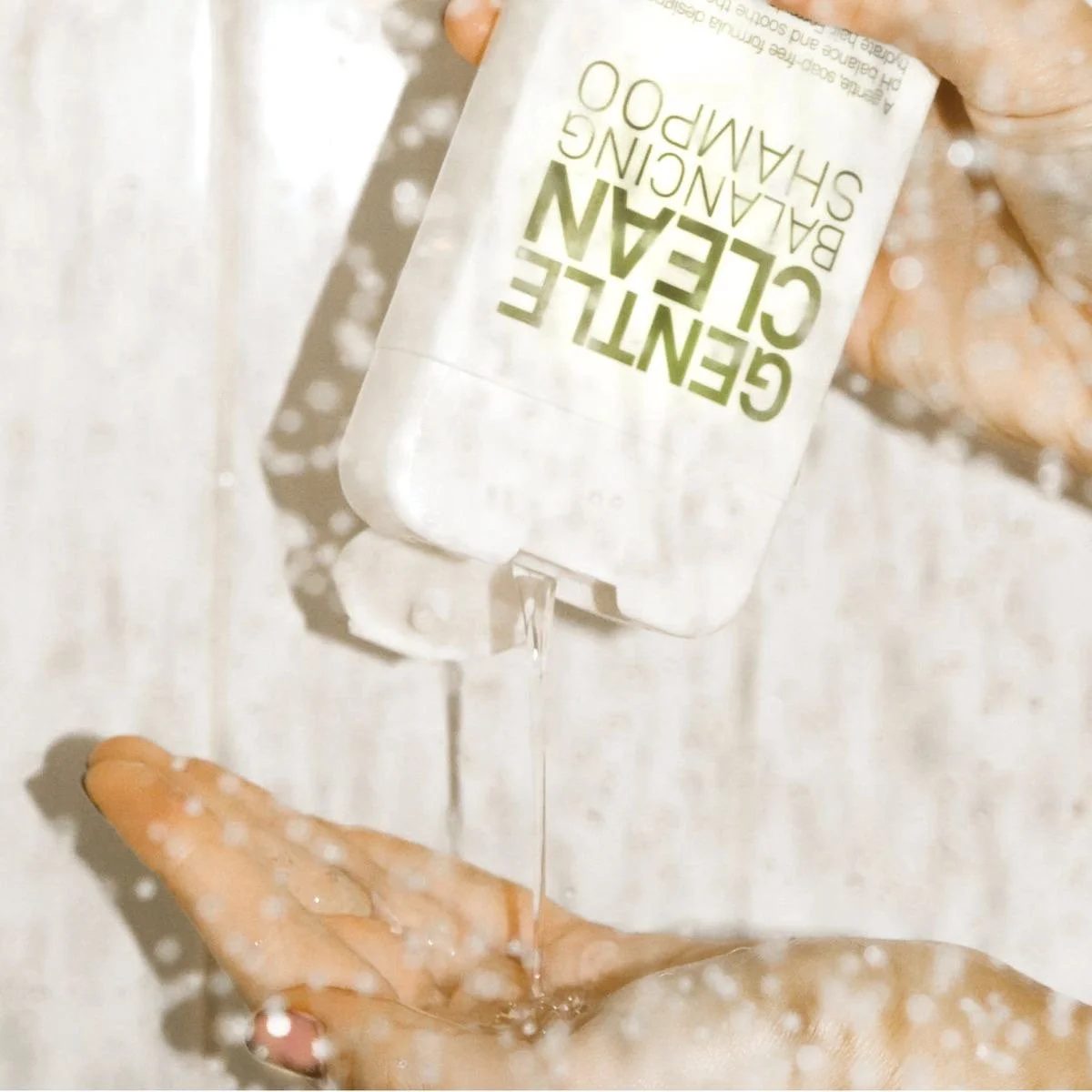 A person holding a bottle of gentle cleansing scrub and squeezing a small amount of foamy product onto their hand.