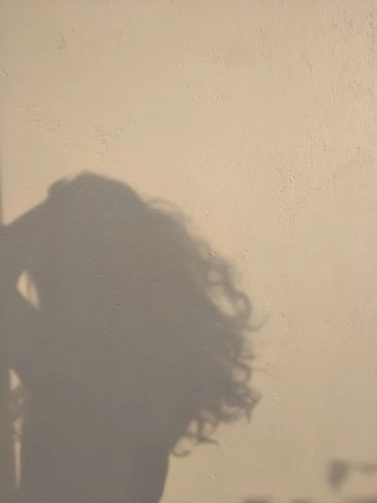 The shadow of a person with curly hair on a beige wall.