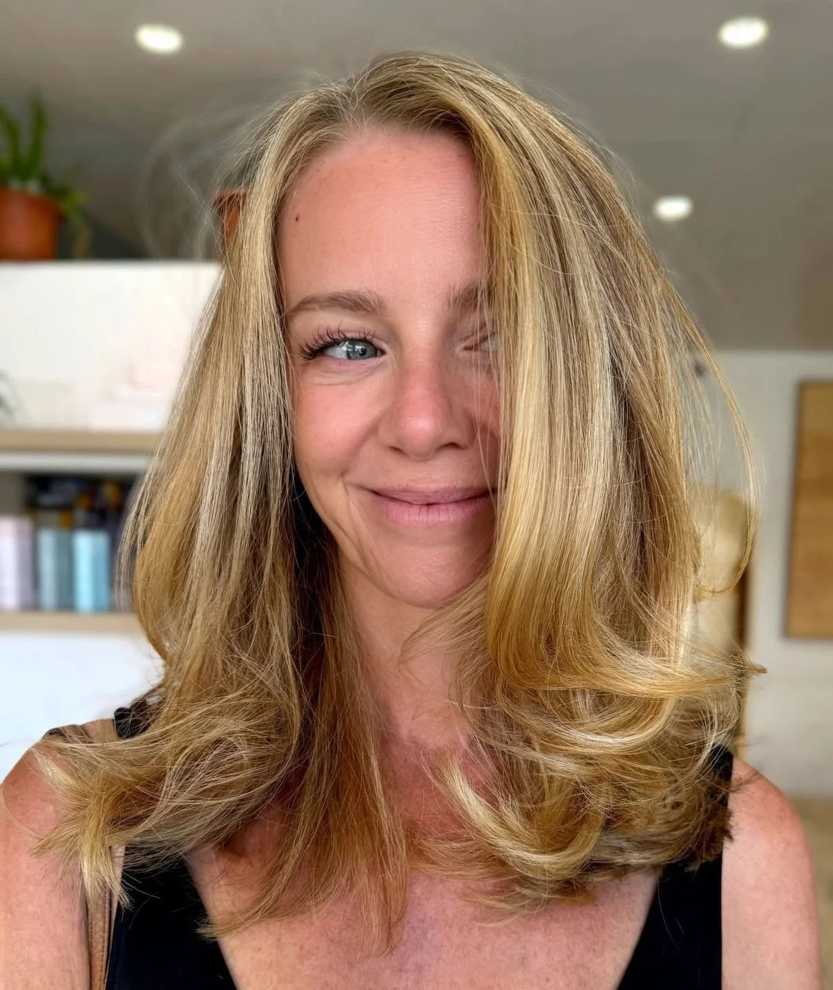 A woman with long blonde hair, fair skin, blue eyes, and a subtle smile, looking slightly to the side in an indoor setting.