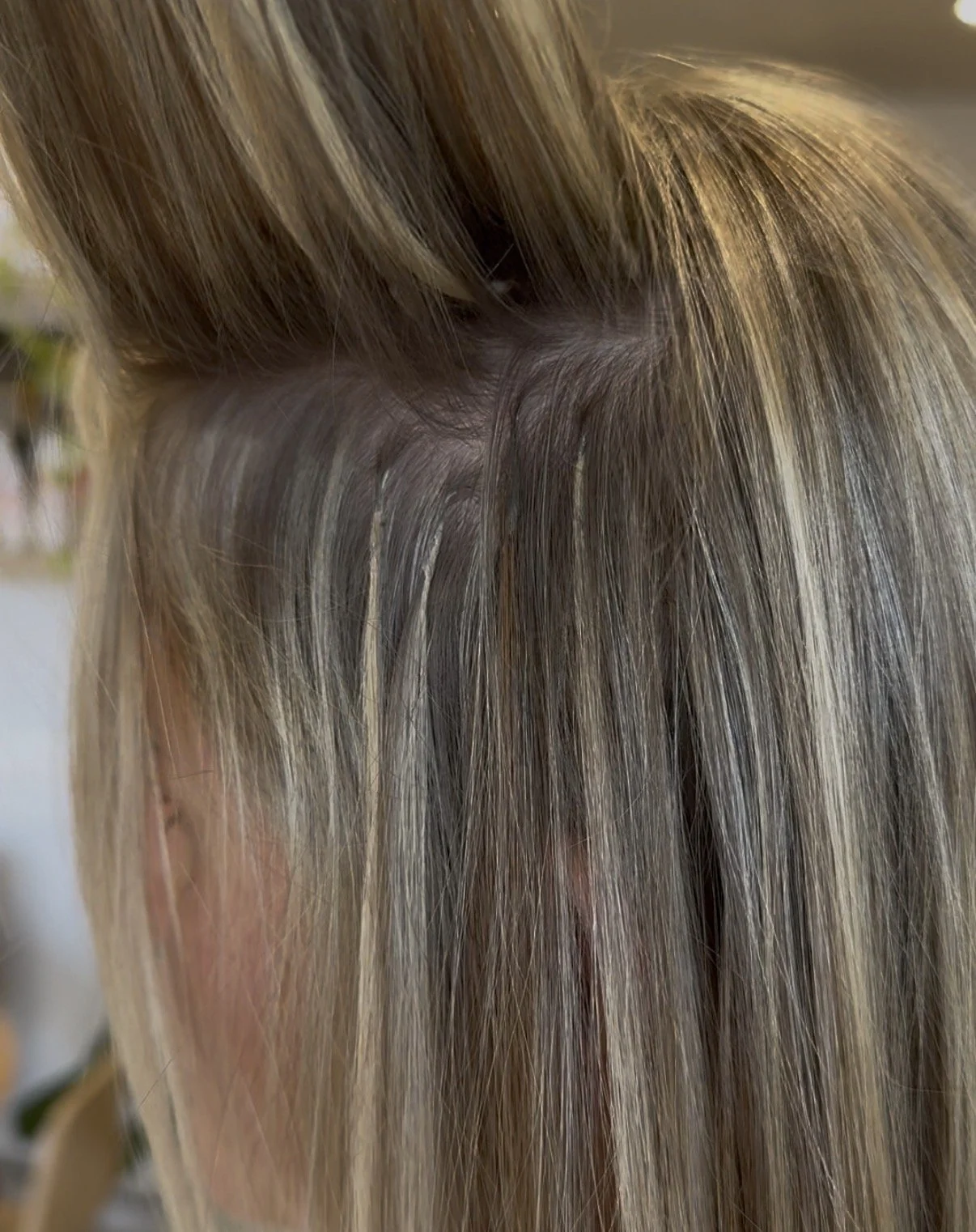 Close-up of a person's head showing blonde and light brown hair with a small section styled up, revealing the roots.