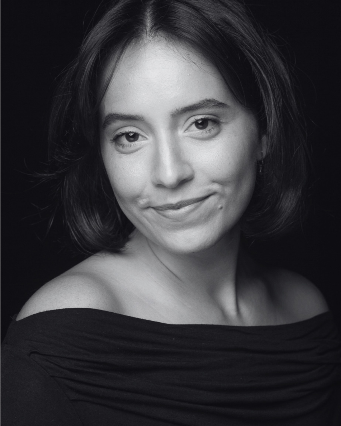 Black and white portrait of a woman with shoulder-length dark hair, smiling softly, wearing an off-the-shoulder top.