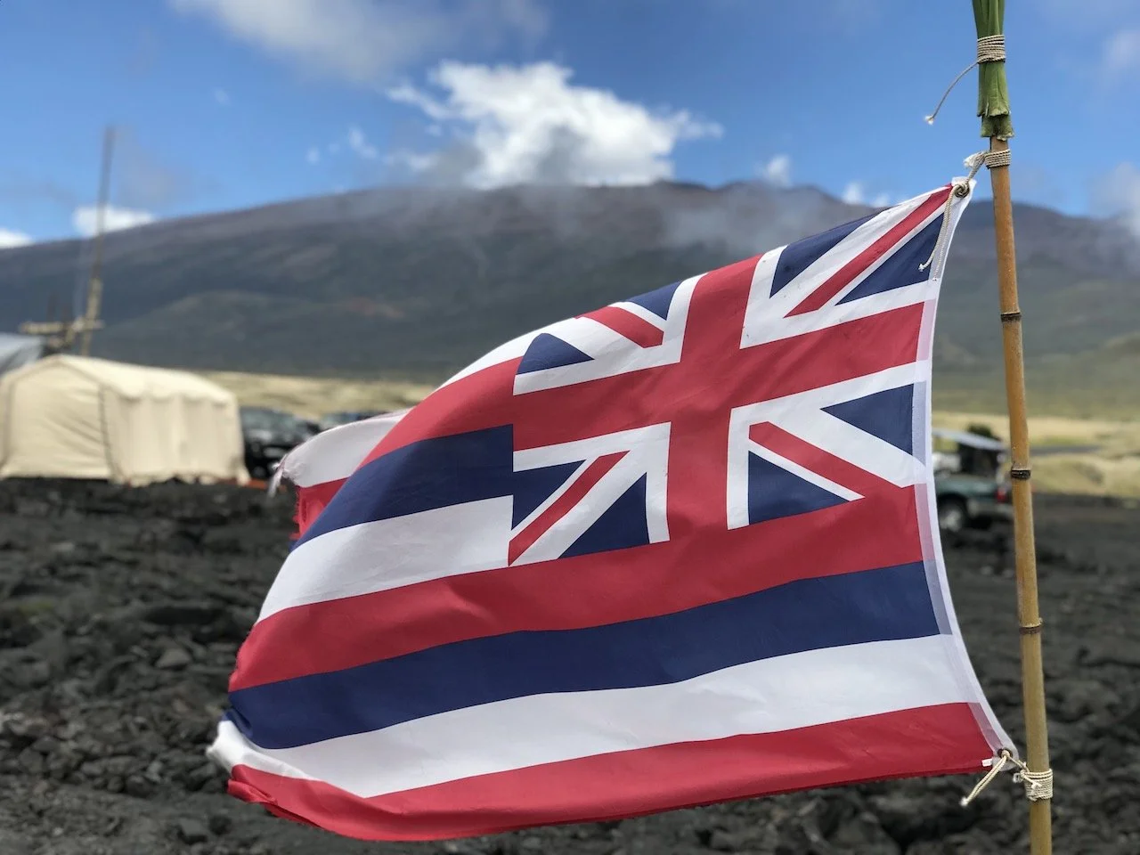 Hawaiian flag on a pole with a mountainous landscape in the background