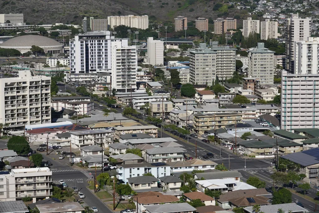A cityscape with numerous mid-rise and high-rise apartment buildings and houses, with a hill or mountain in the background.