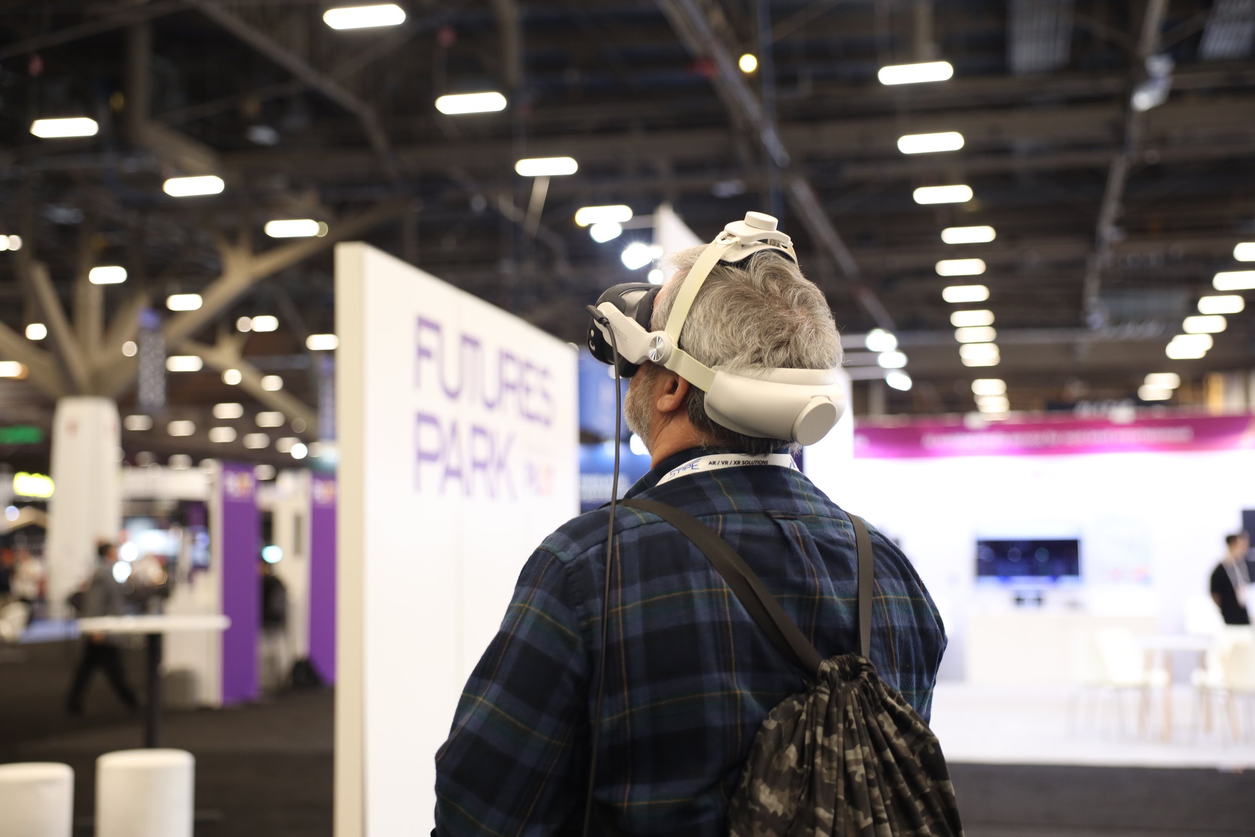 A man with gray hair and a beard wearing a virtual reality headset at an indoor tech event.