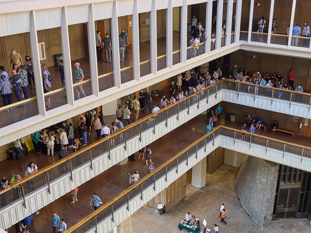 Multiple floors of a large, busy building with people walking, sitting, and gathering in common areas and hallways.