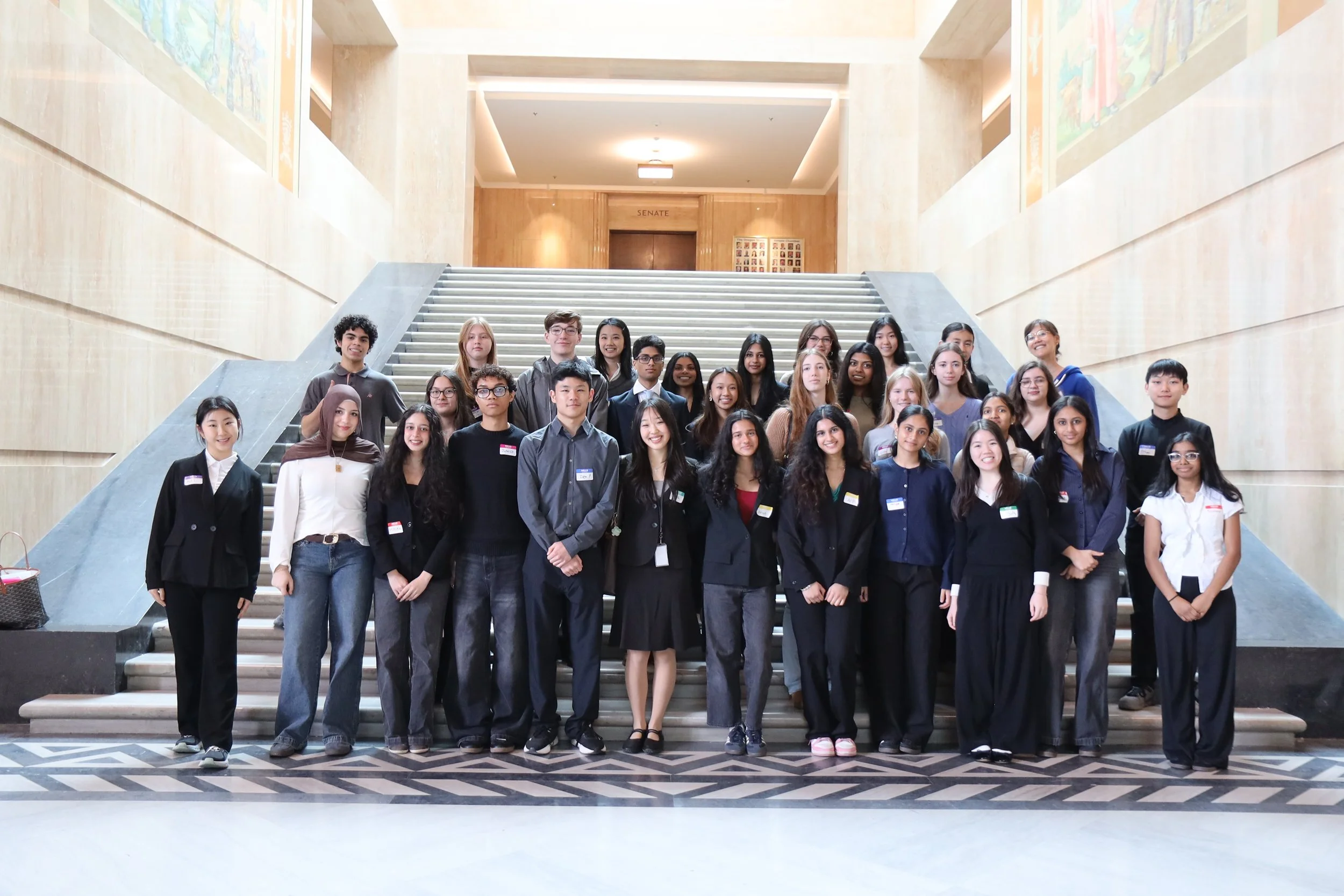 Group of diverse young adults standing on stairs inside a building, smiling at the camera.