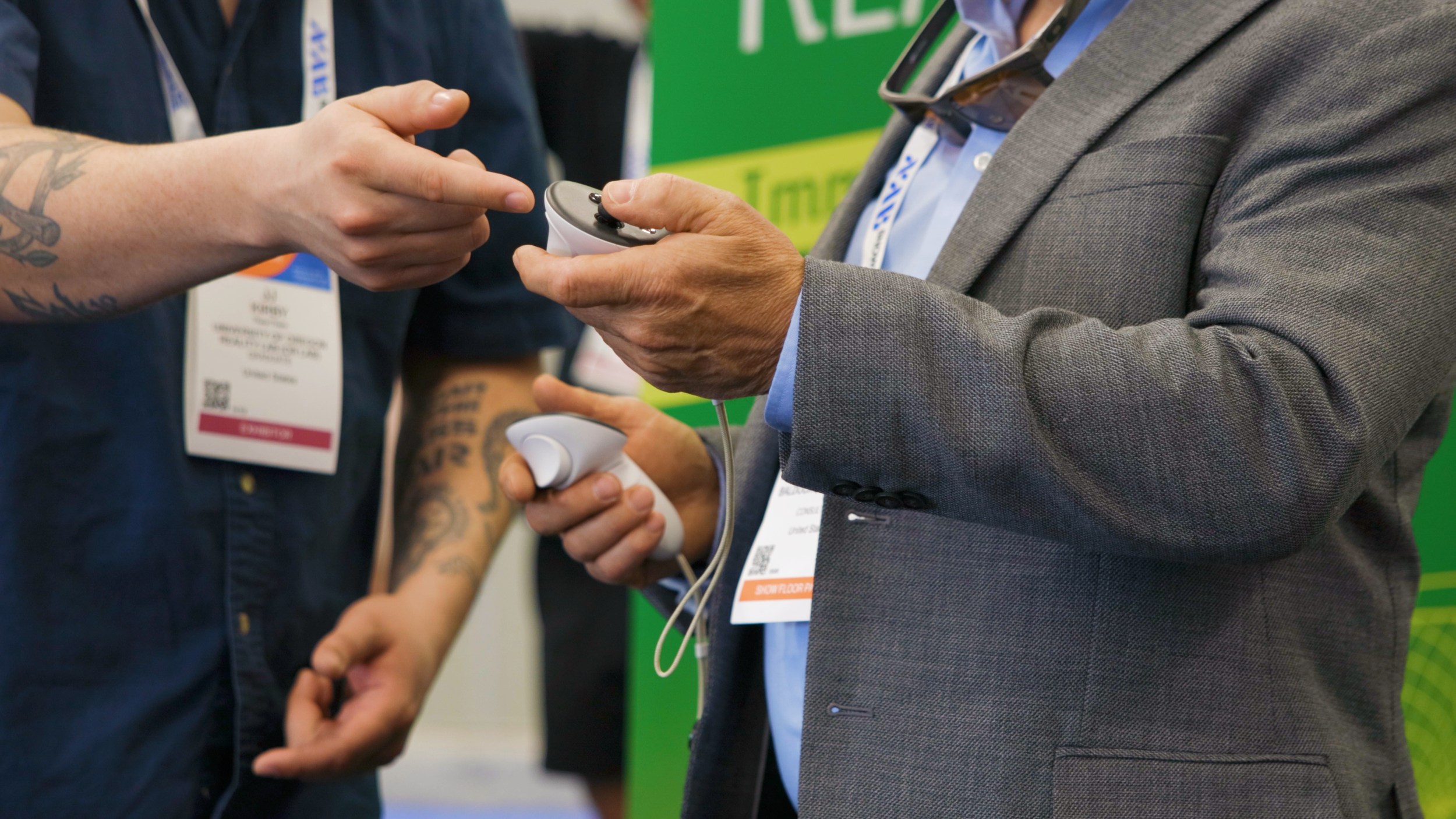 Two men are exchanging or displaying a device related to healthcare or technology, with visible conference or trade show badges.