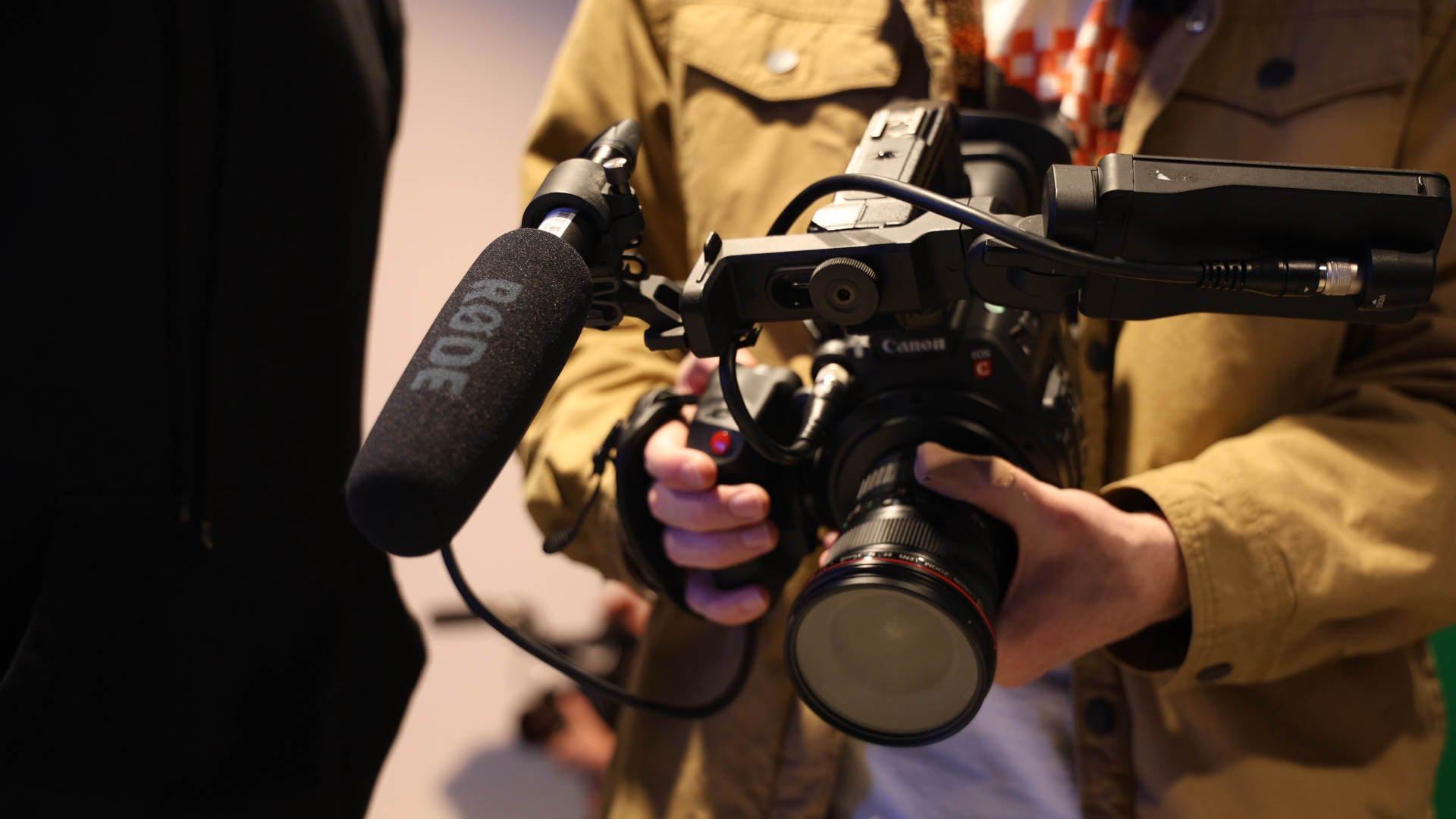 Person holding a professional video camera with a mounted microphone in a close-up shot.