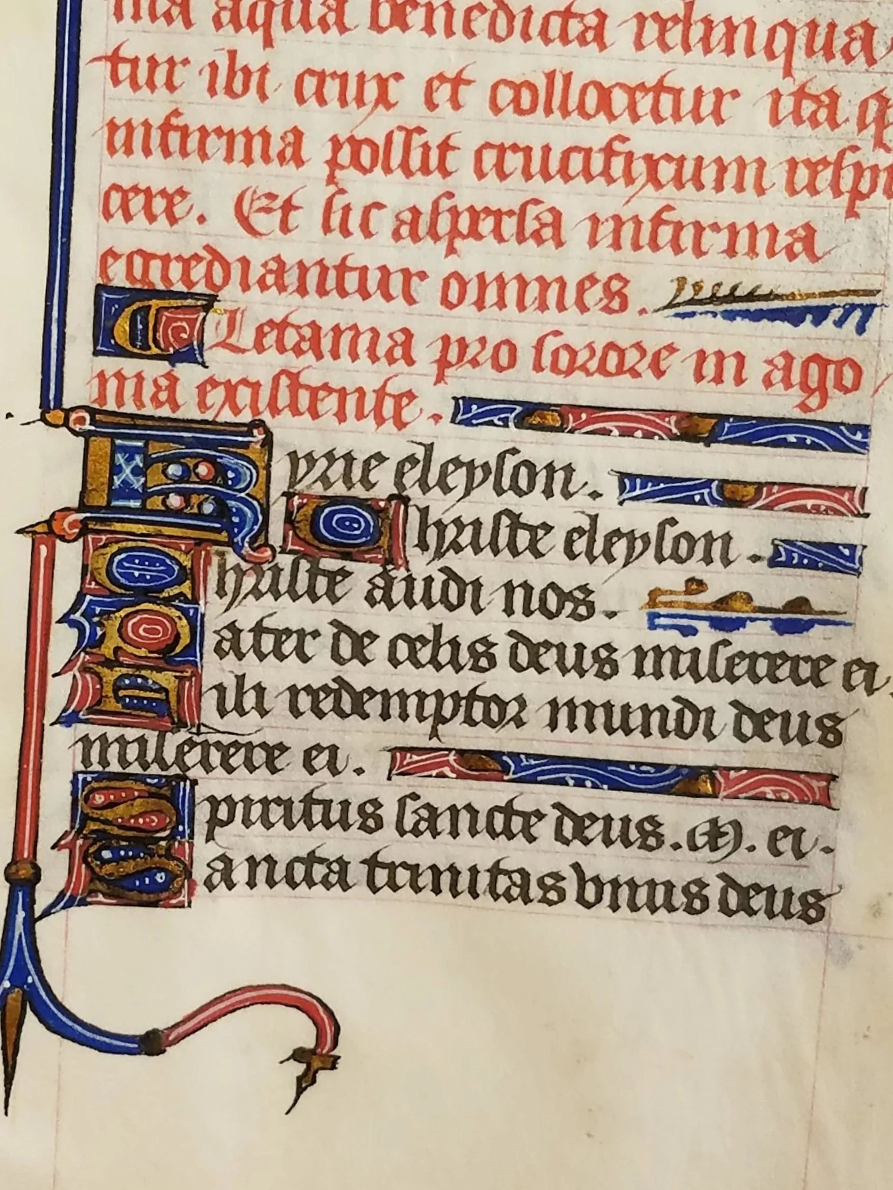 Page of a medieval illuminated manuscript with Latin text in red and black ink, decorated initials with gold accents, and colorful margins featuring floral and geometric patterns.