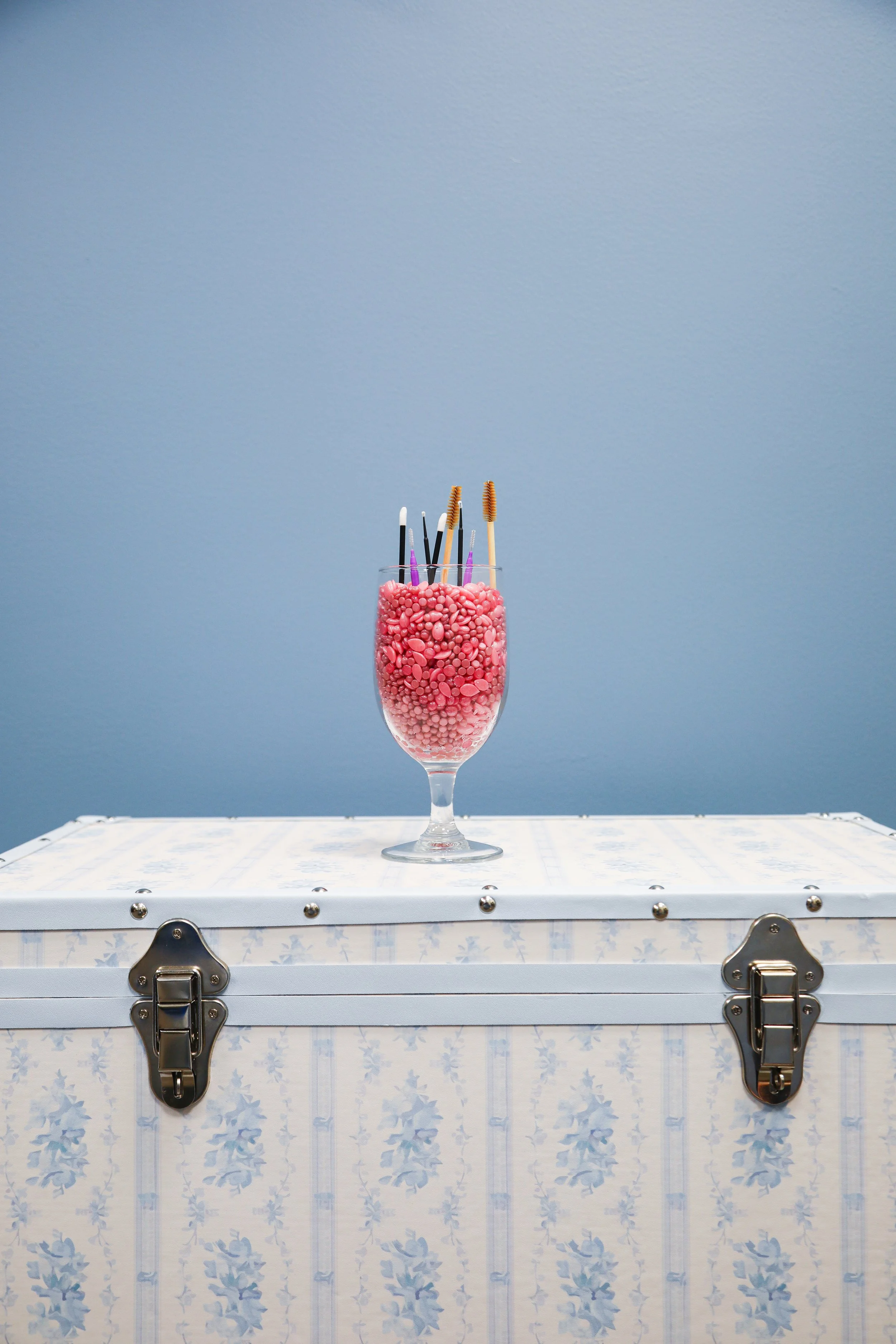 wine glass filled with wax beads, spoolies, lip brushes, small brushes on treasure chest