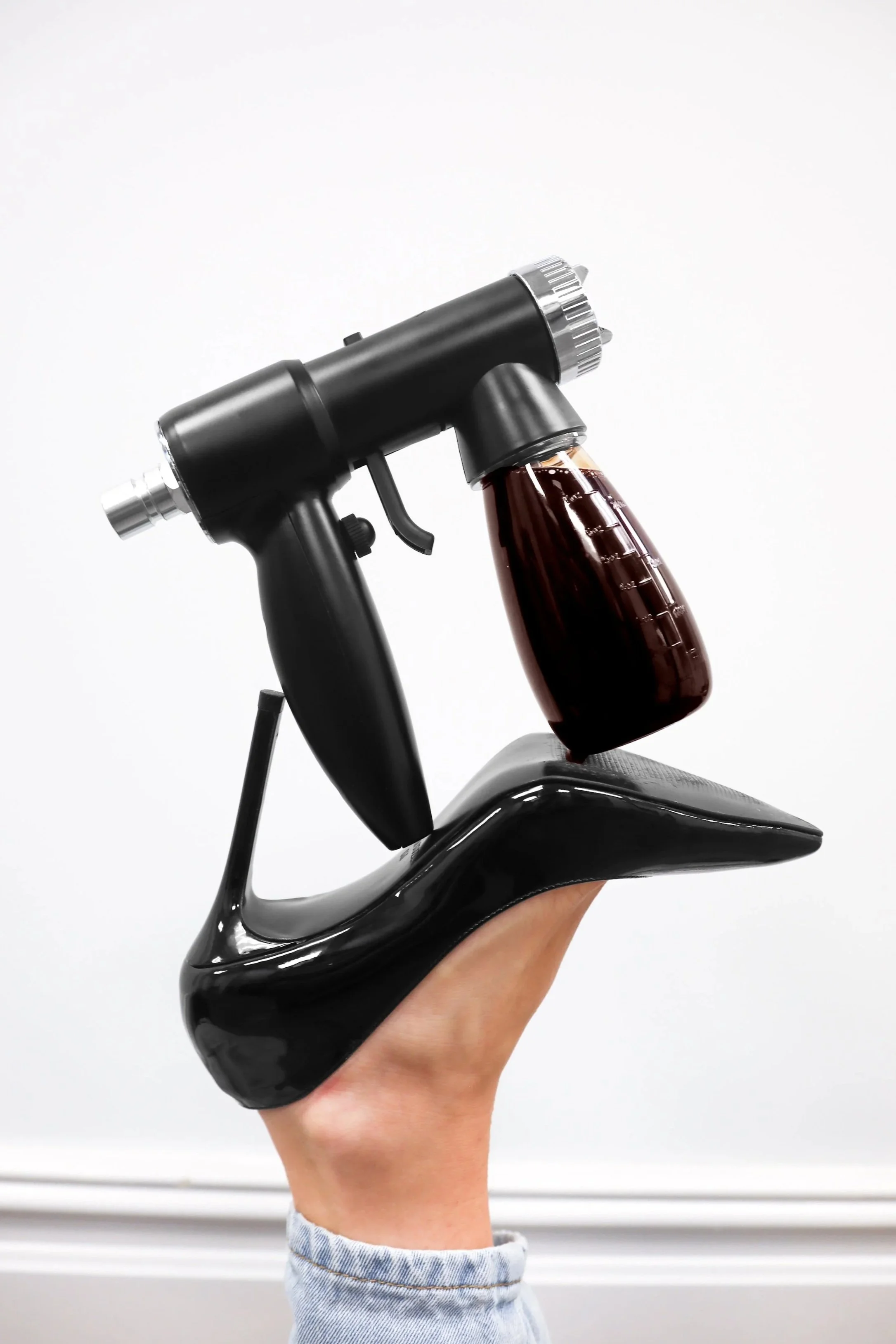 spray tan gun balancing on black steve madden heel