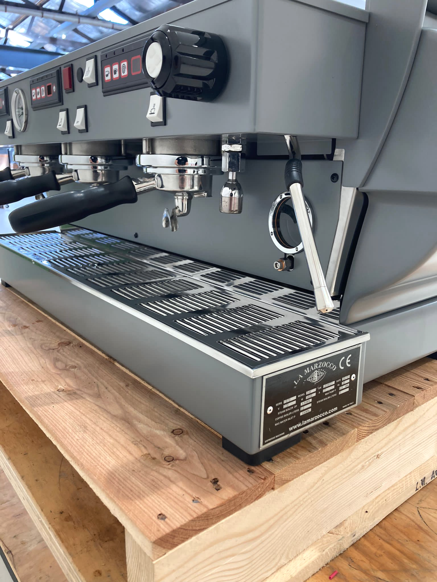 A commercial espresso machine on a wooden table in a warehouse or industrial setting.