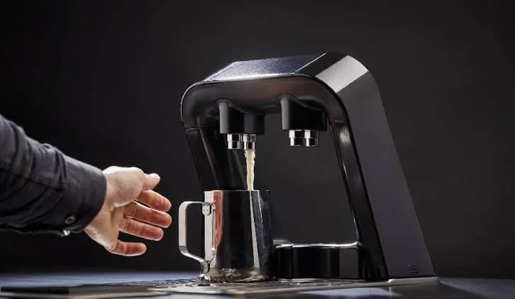 Person pouring water into a glass under a modern black water dispenser with two spouts.