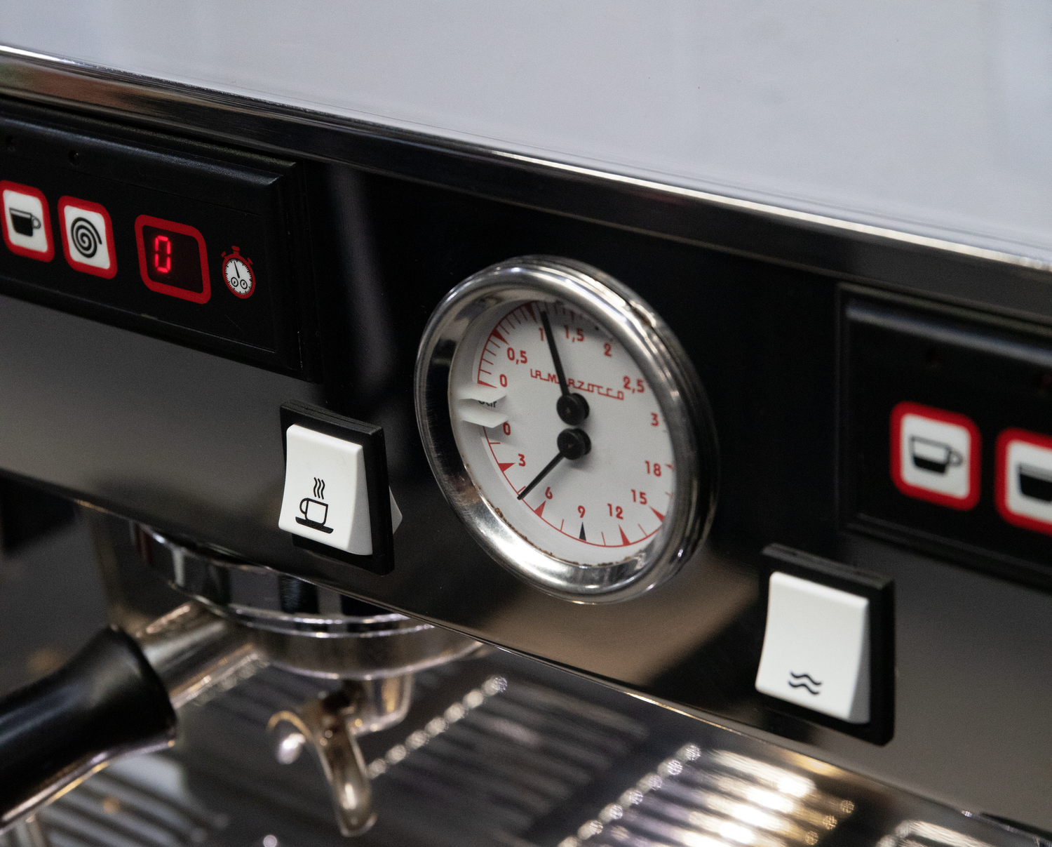 Close-up of a coffee machine control panel featuring a timer gauge, hot water button, and steam button.