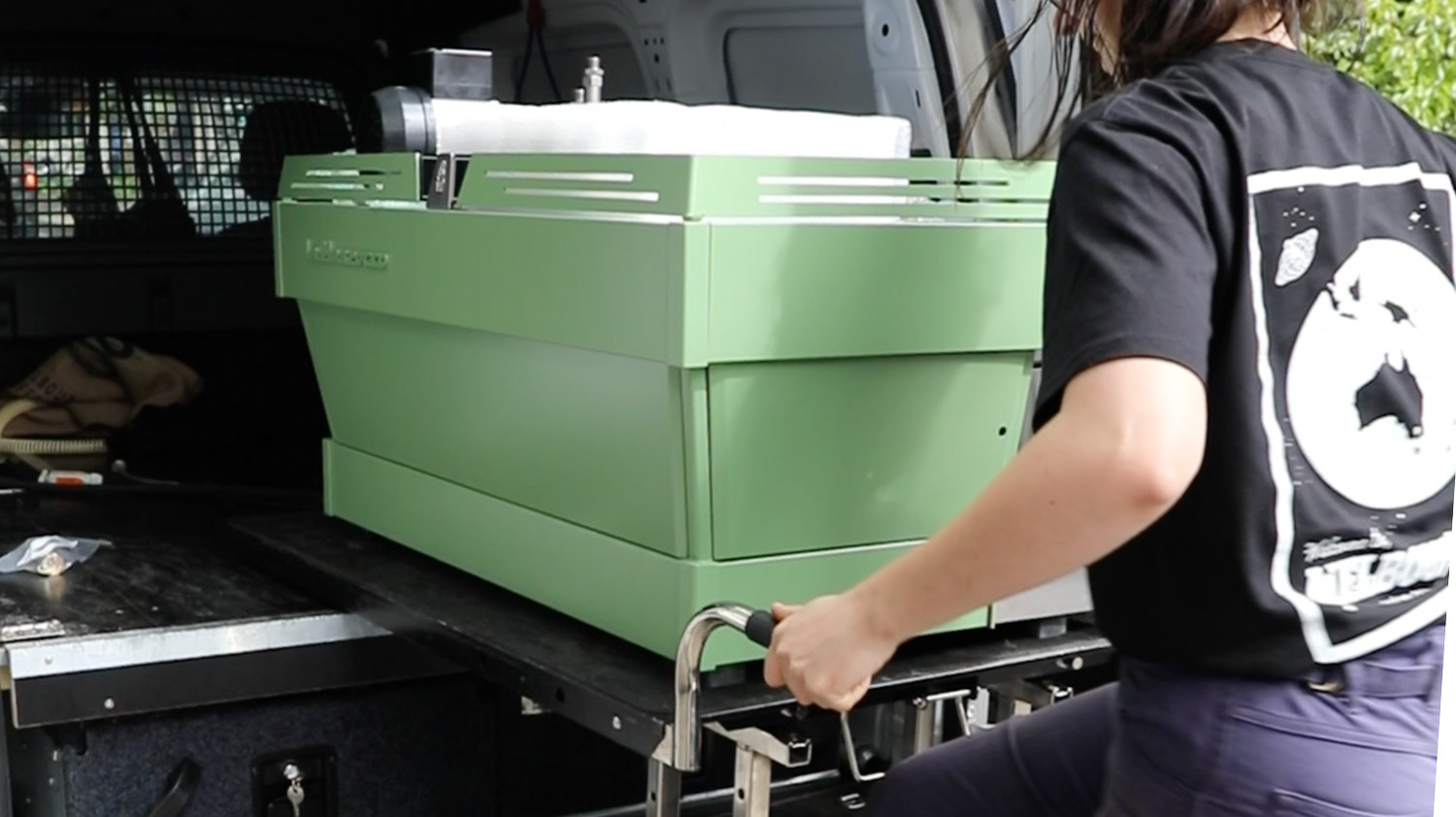 A person in a black T-shirt operating a green cannabis extraction machine in a vehicle's cargo area.